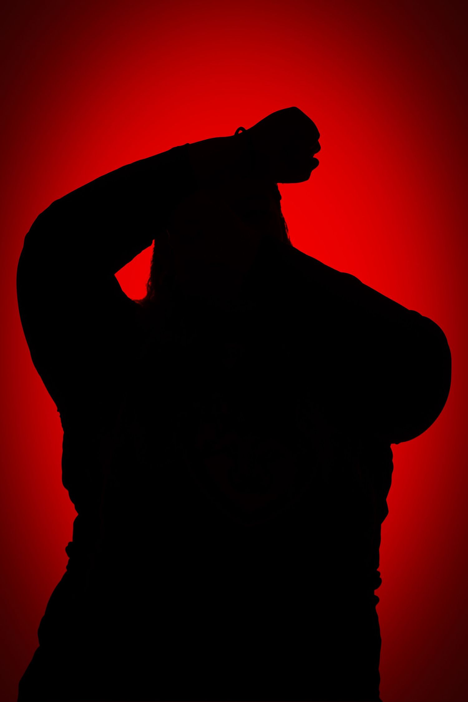 Dramatic silhouette of a person with arms raised and bent behind their head against a deep red gradient background.