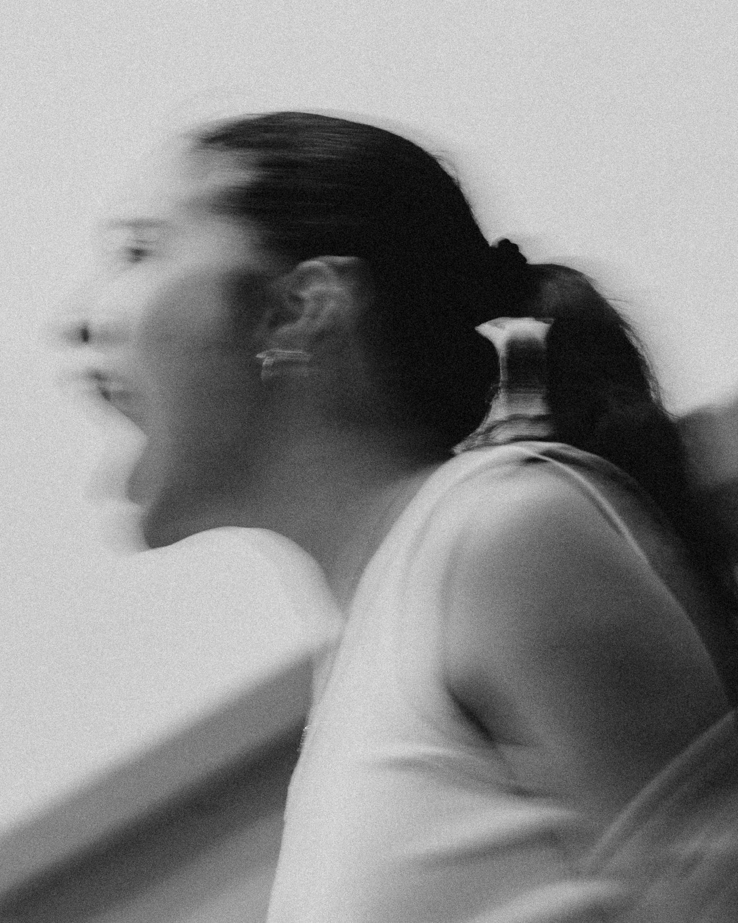 Black and white motion-blurred photo of a woman with a ponytail shouting or cheering with intense emotion.
