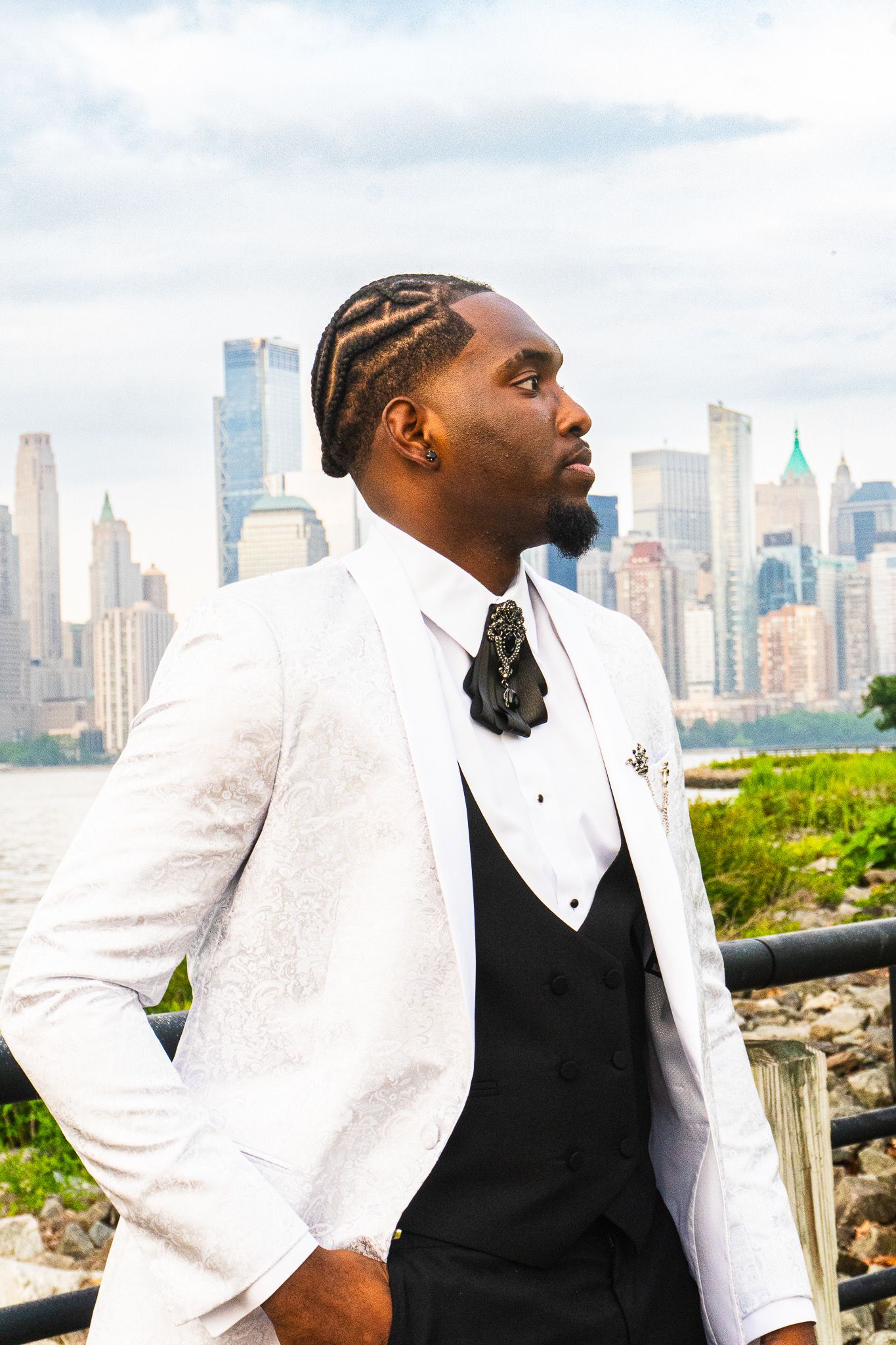 Man in a white jacquard tuxedo jacket and black bow tie stands in profile with the city skyline behind him.