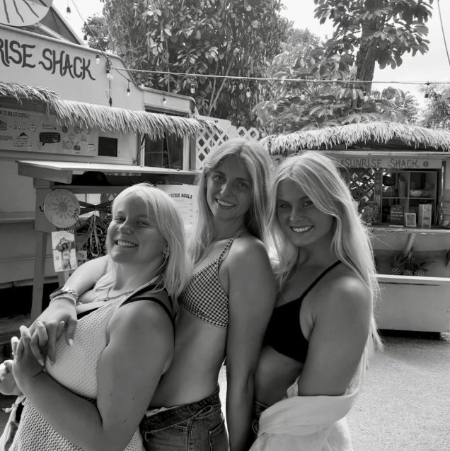 Group of friends posing together outside a beach shack on a sunny day.