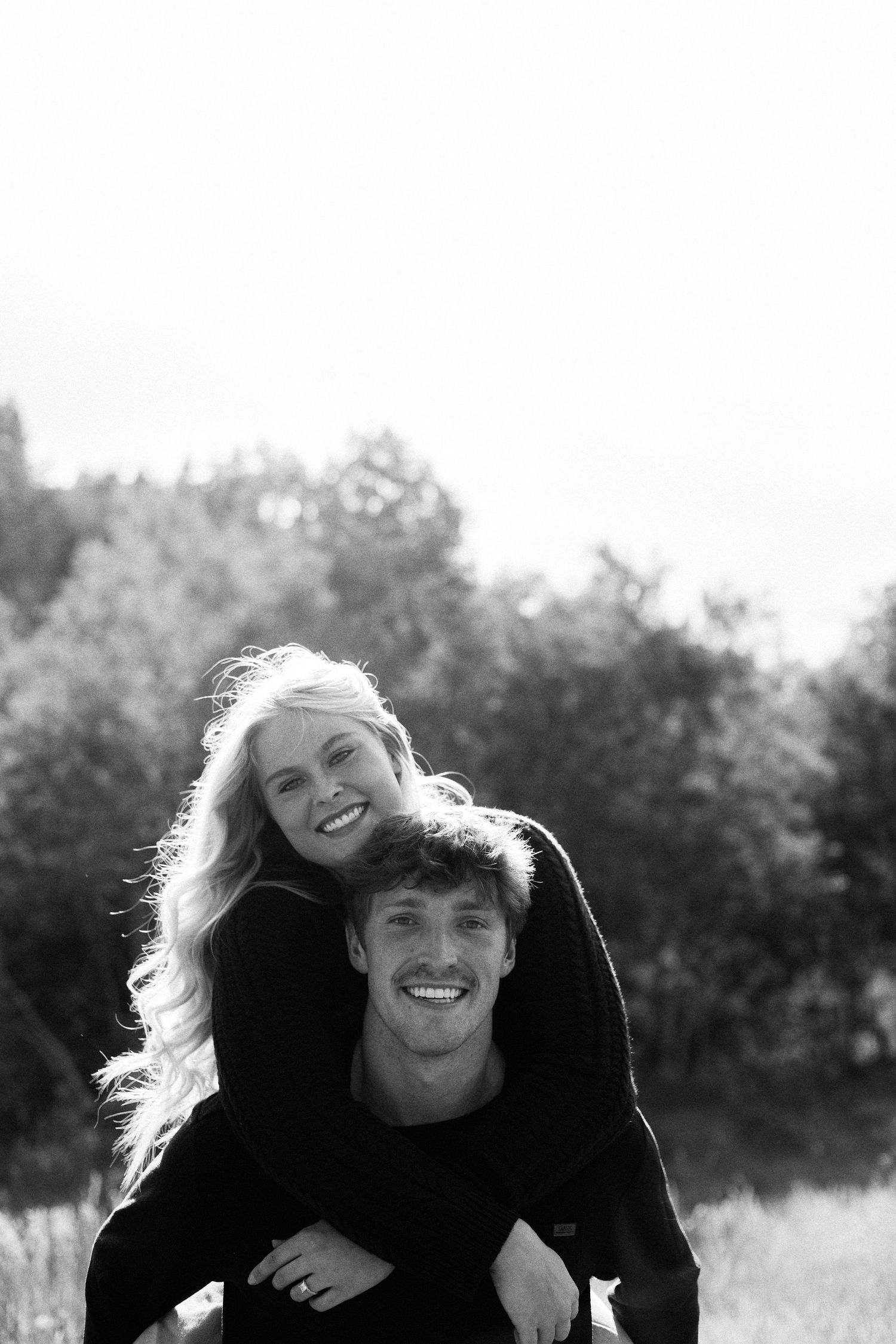 Black and white portrait of a couple sharing a playful moment outdoors.