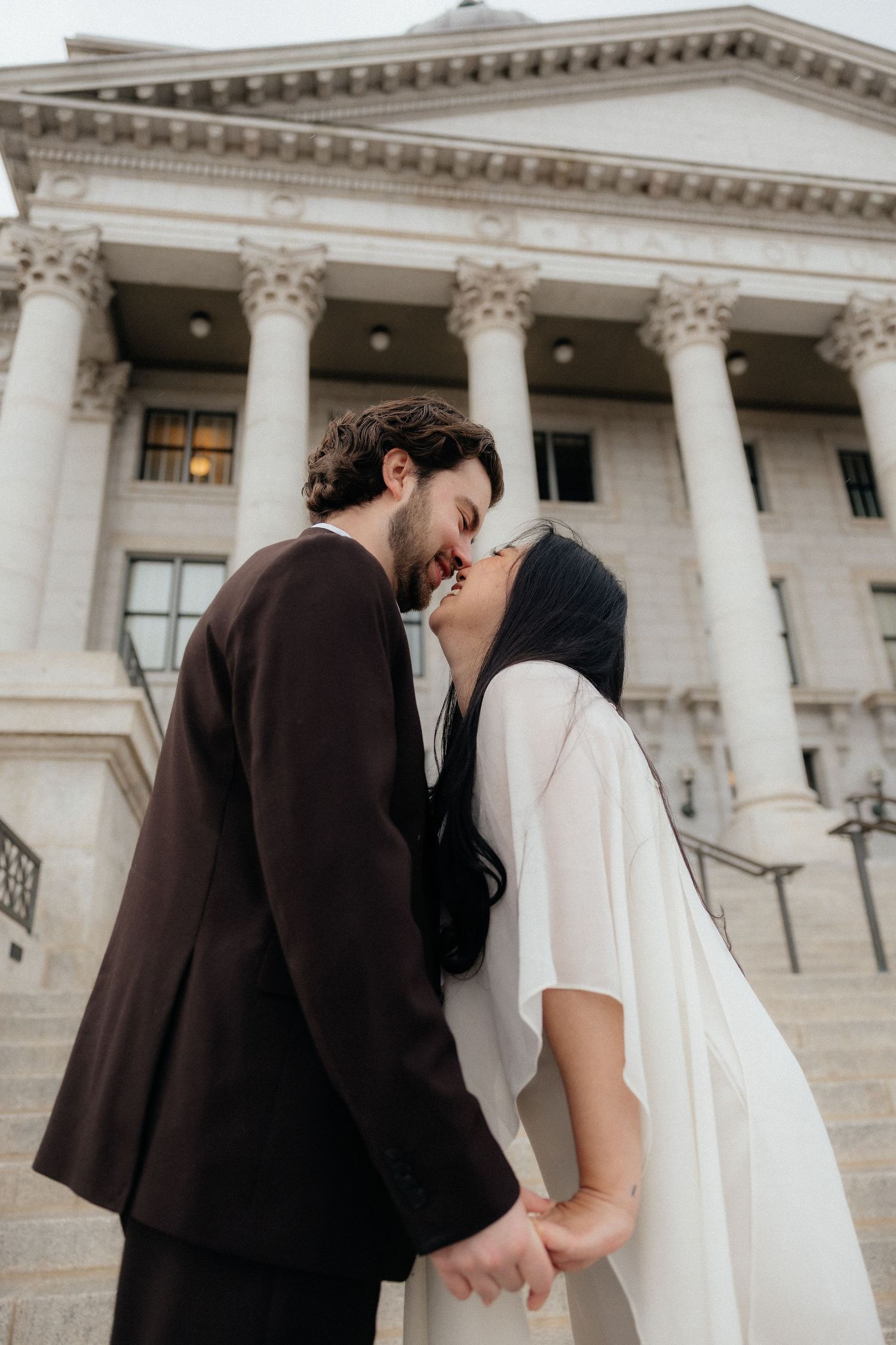 A couple embracing in front of a grand, columned building, conveying a romantic and intimate moment.