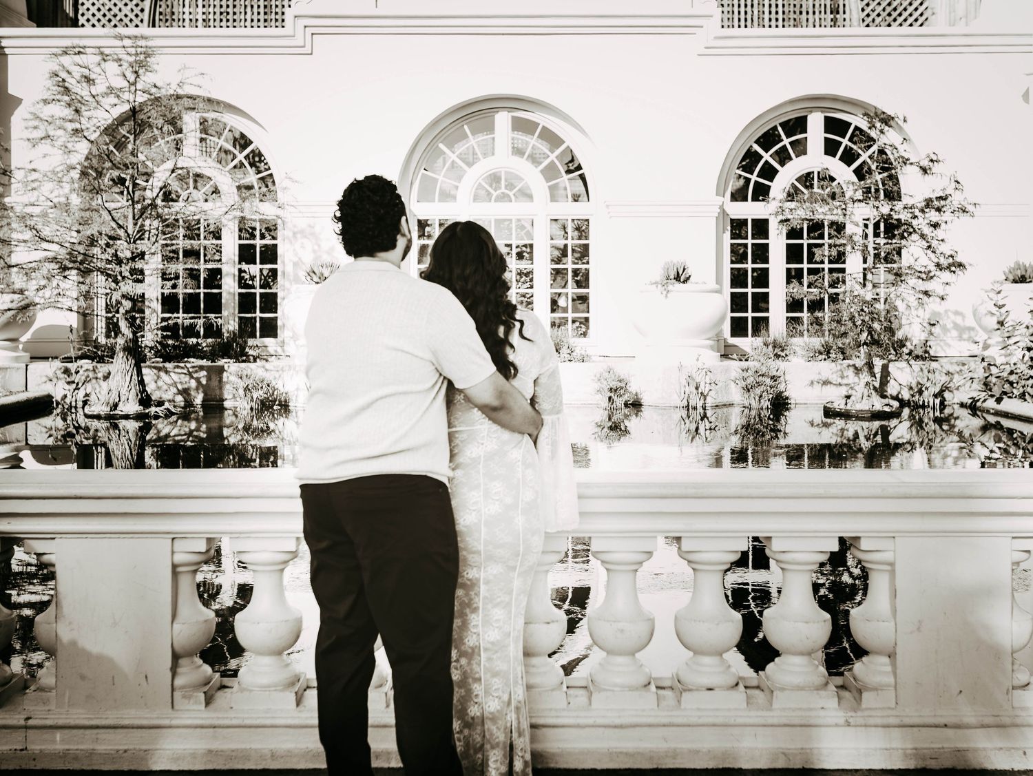 poignant black-and-white image of an engaged couple embrace with their backs to the camera as they face a beautiful building at Balboa Park
