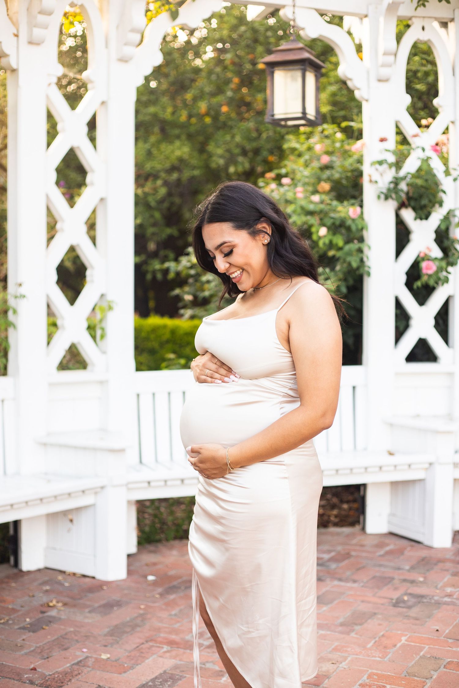 Pregnant woman holding her baby bump and smiling as she looks at the baby bump during a maternity session at the Los Angeles Arboretum