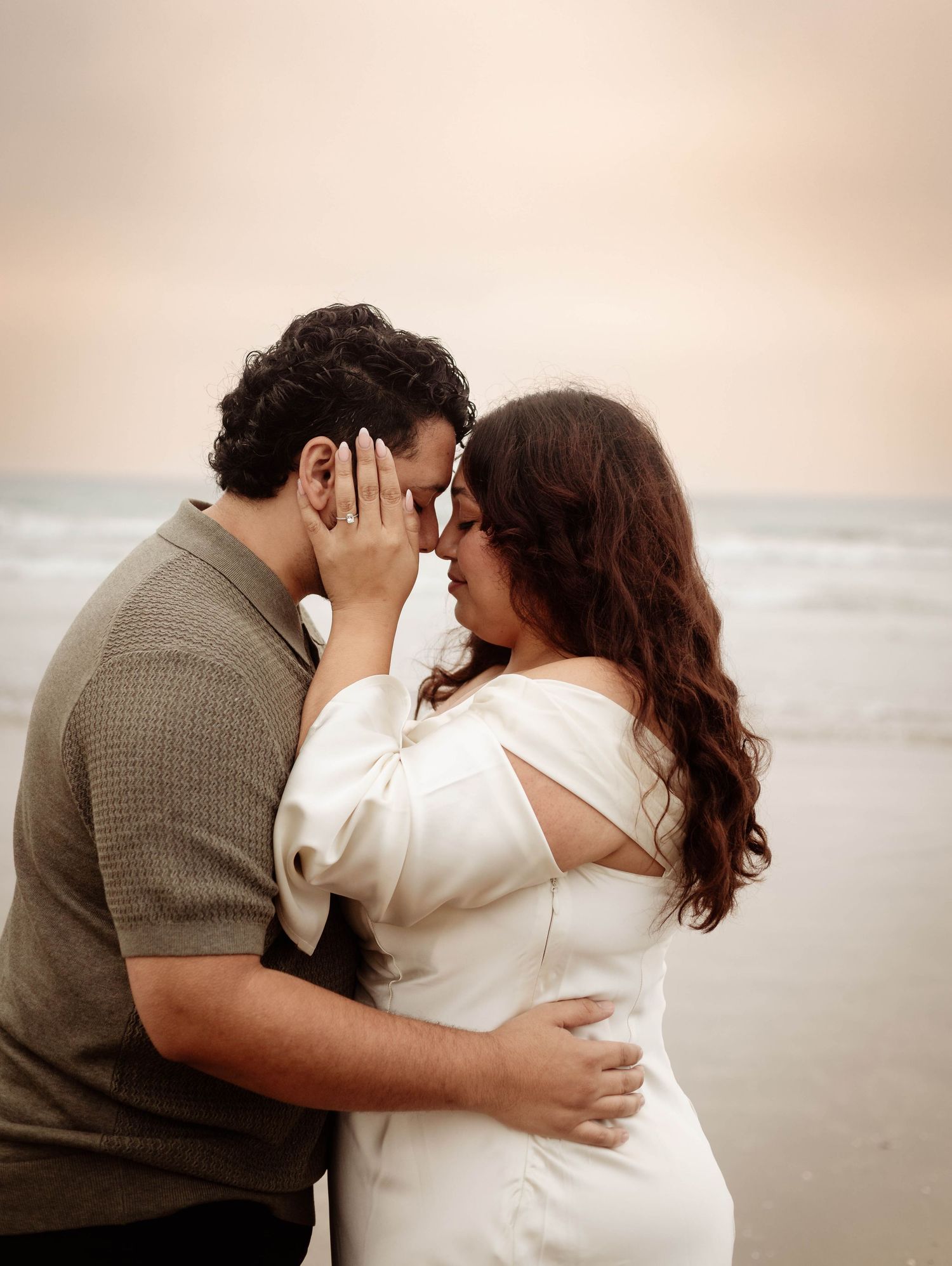 Scripps Pier, San Diego Beach Engagement Portrait; couple on beach, in an intimate embrace; she is wearing an elegant white dress