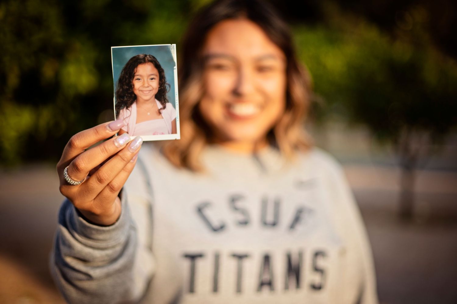 CSUF Titans student holds up childhood school photo smiling outdoors on campus.