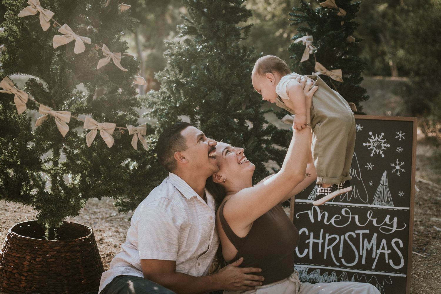 Family laughing together outdoors during a Christmas mini session with a Merry Christmas chalkboard sign.