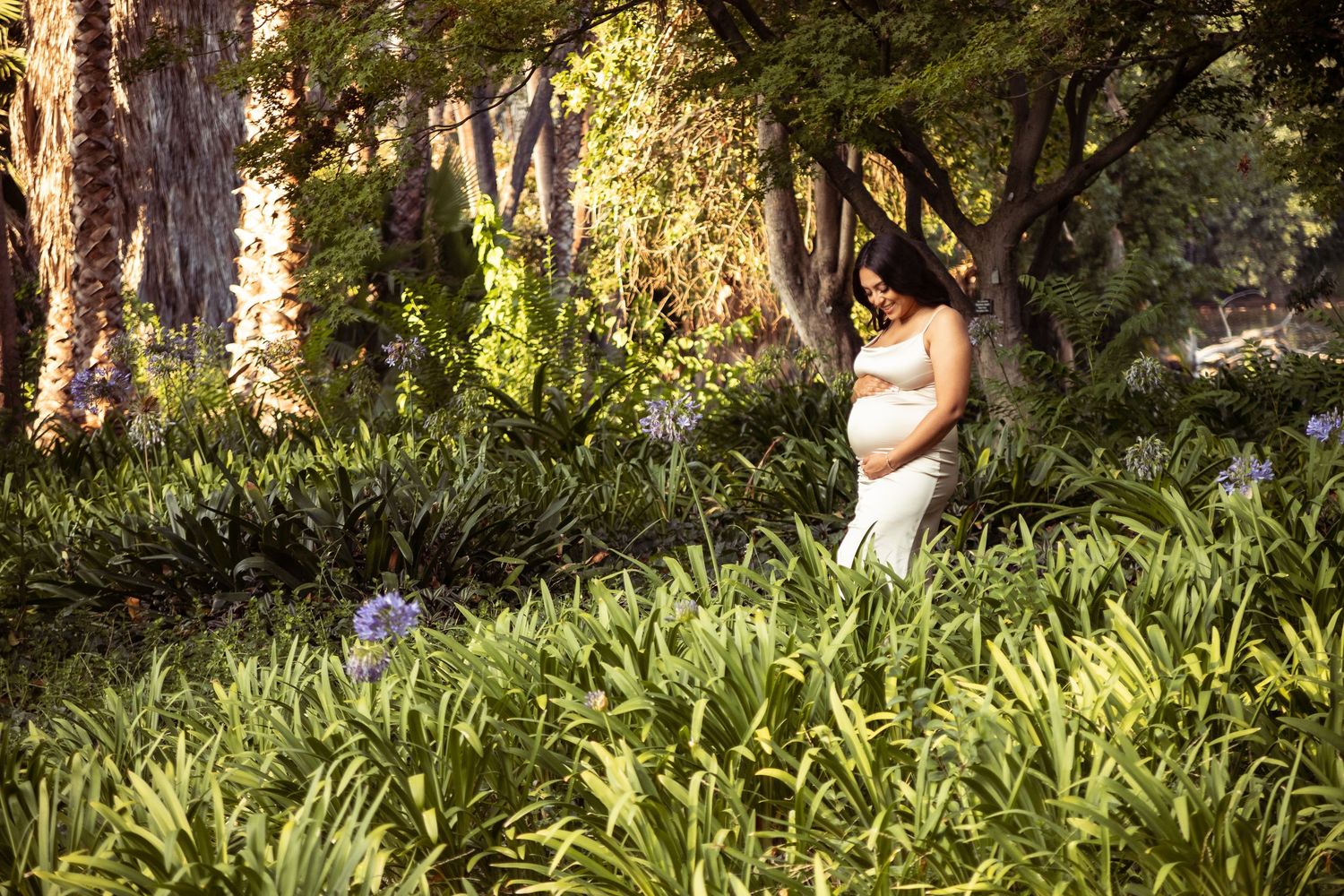 Expectant mother standing in a green field, smiling and gazing at her baby bump during a maternity session at the Los Angeles Arboretum