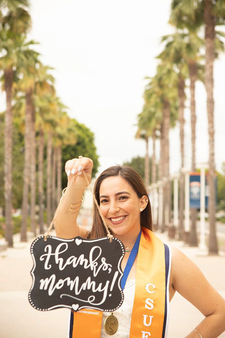 CSUF graduate with graduation sash smiling at camera holding a 