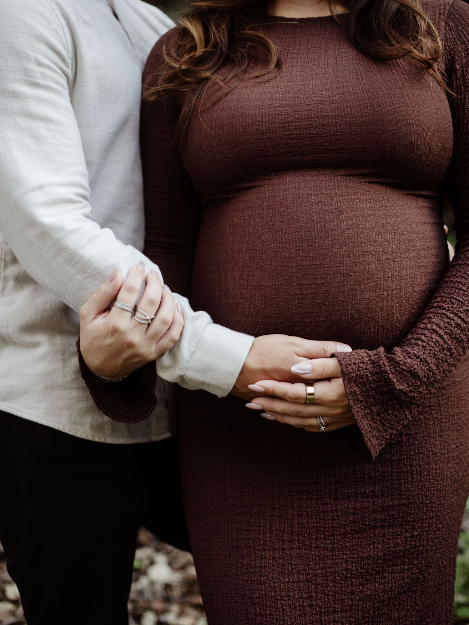 close up of baby bump as the father touches the baby bump, and the woman holds his hand. Woman is wearing a deep burgundy dress.