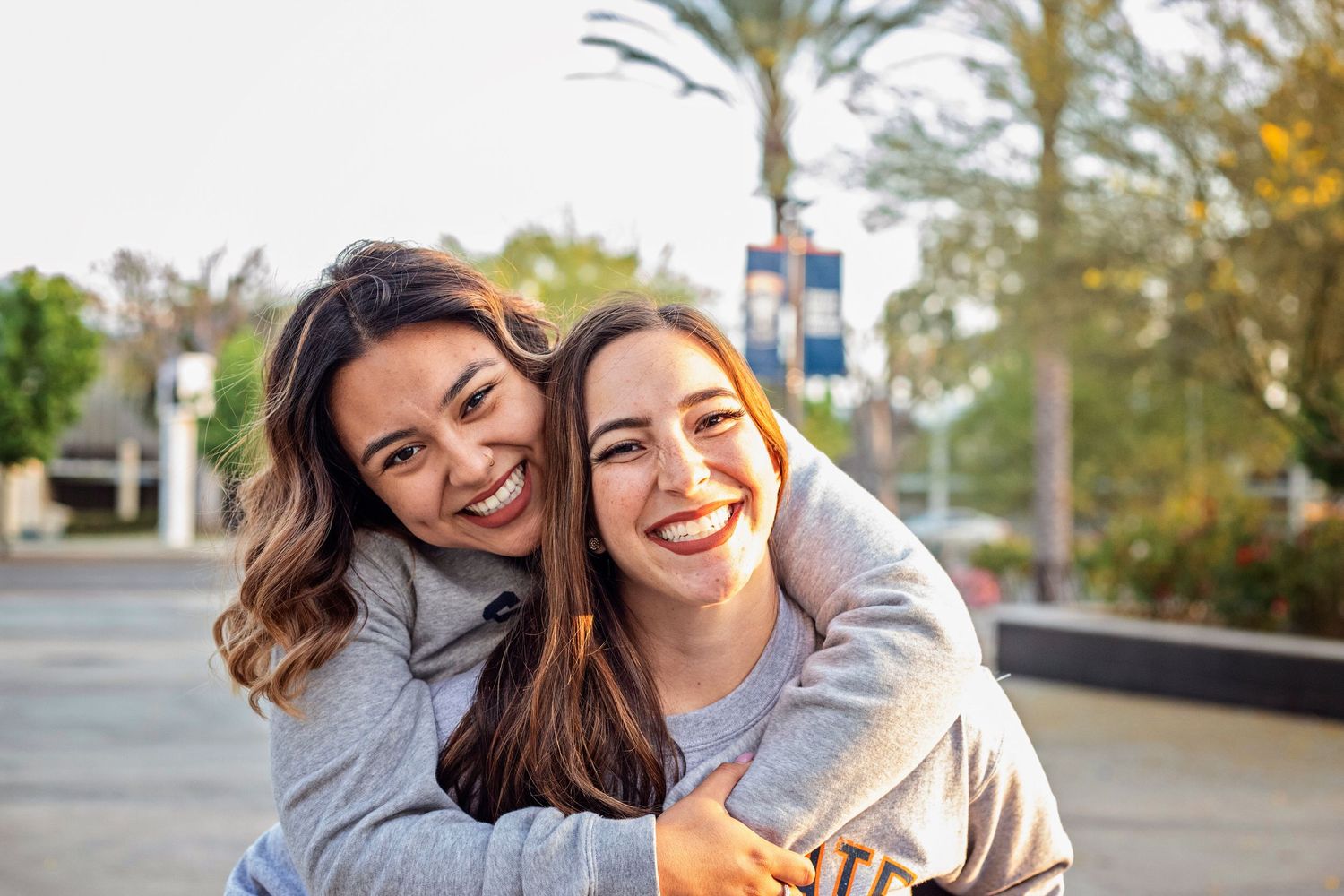 Two young friends on the CSUF campus are laughing and embracing as they look at the camera during a sunset graduation portrait session.