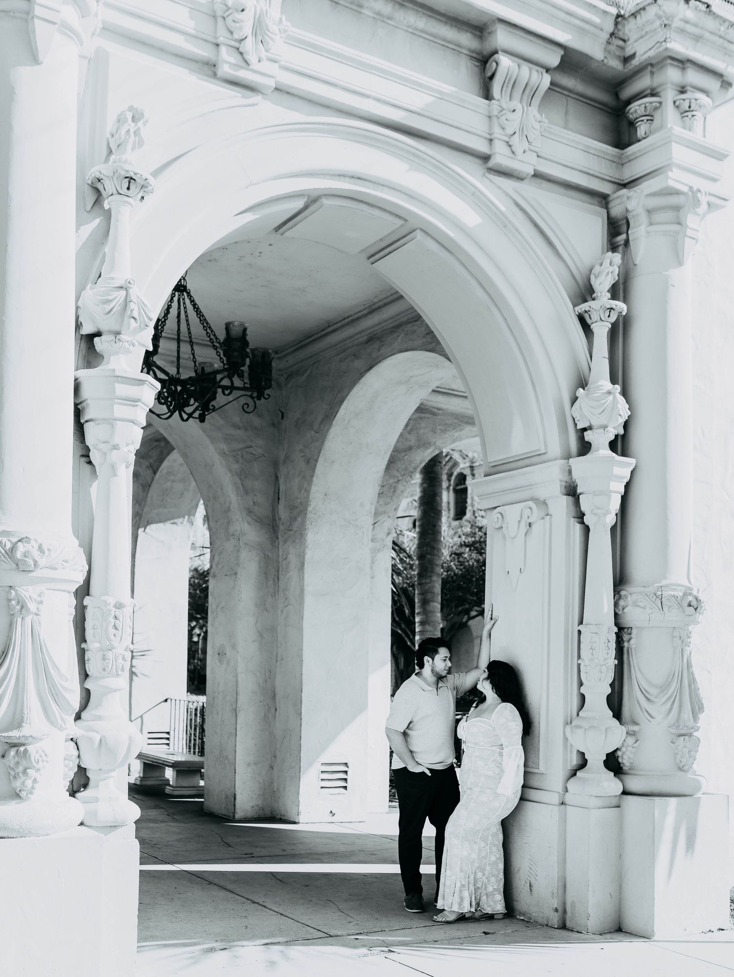 Black and white photo of a couple standing under ornate arched columns at Balboa Park, San Diego.