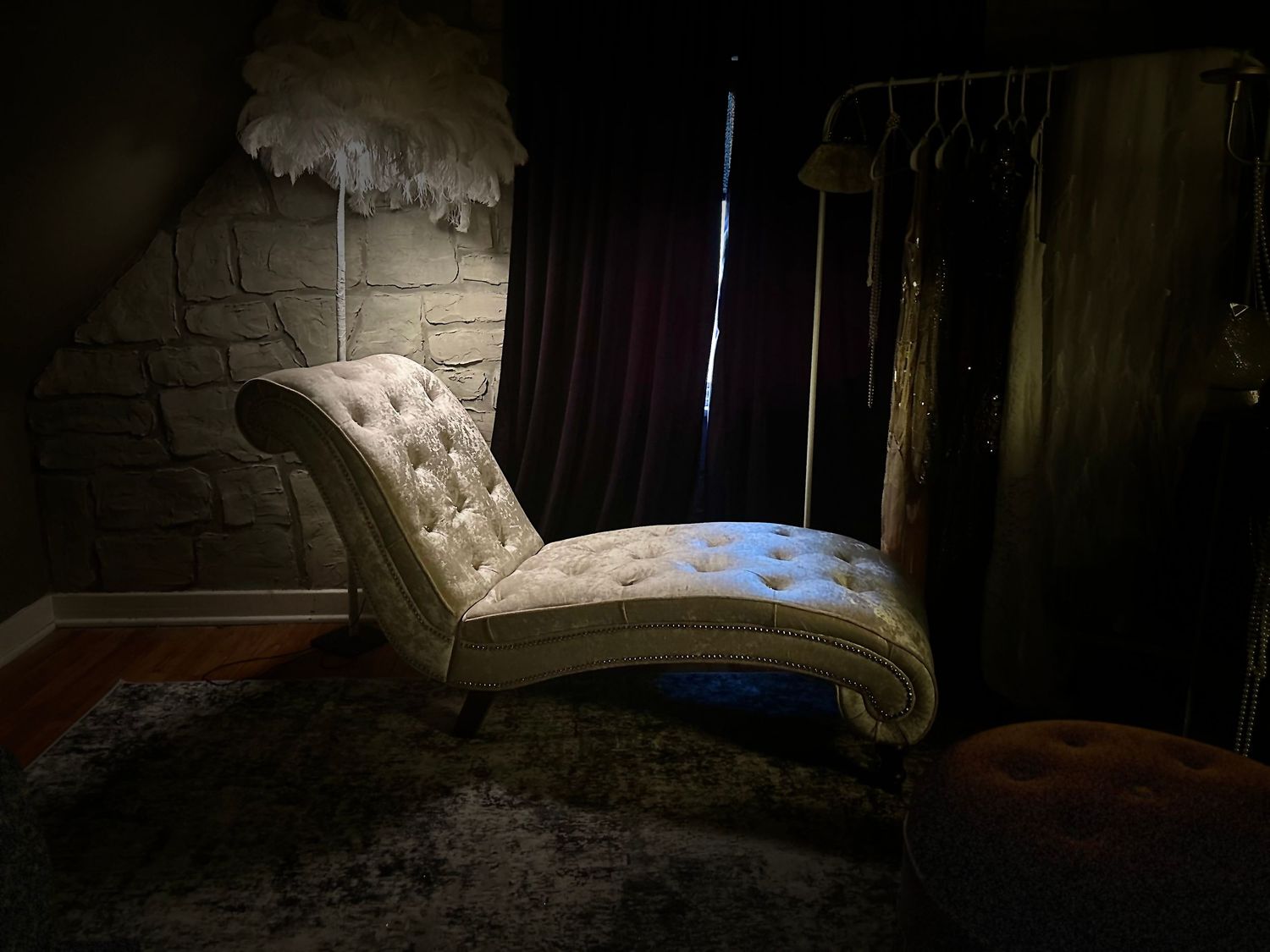 Vintage tufted chaise lounge illuminated by dramatic lighting against stone wall in dark moody setting.