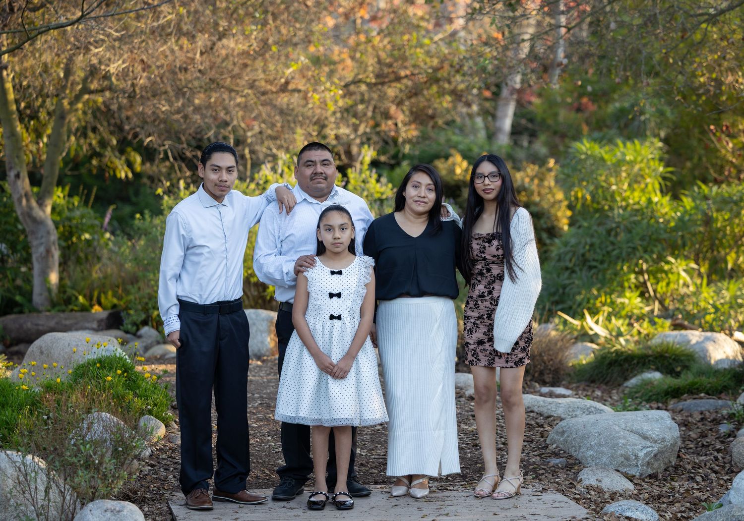 A group poses together outdoors in a garden setting with rocks and autumn foliage in the background.