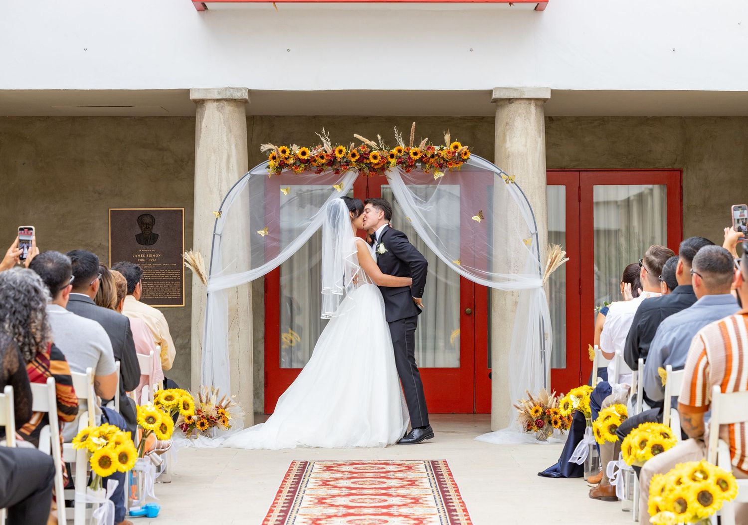 A wedding ceremony setup in a modern venue with bright yellow sunflower decorations along the aisle.
