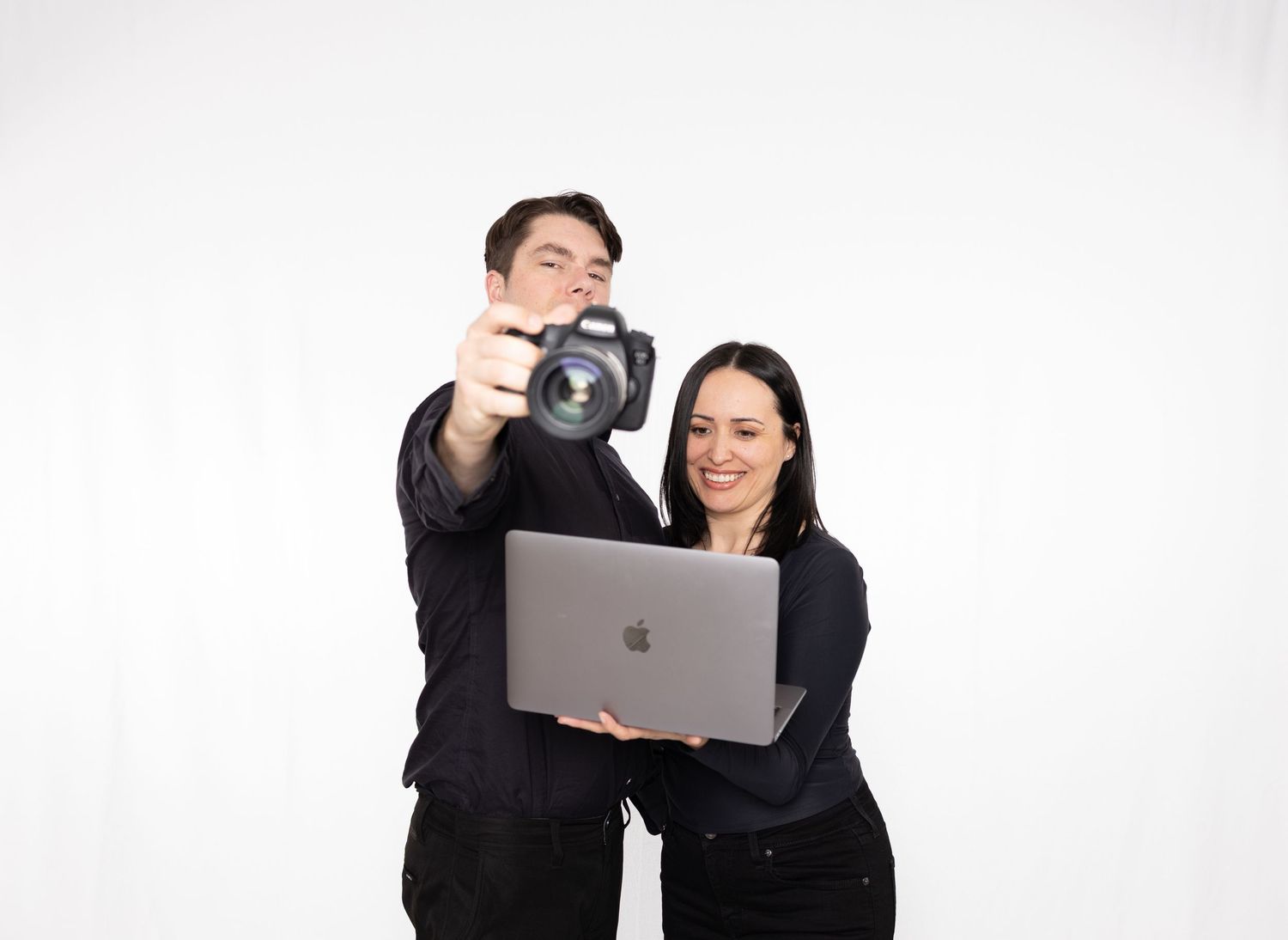 Business professionals in black attire collaborating with laptop and camera while working together in studio setting.