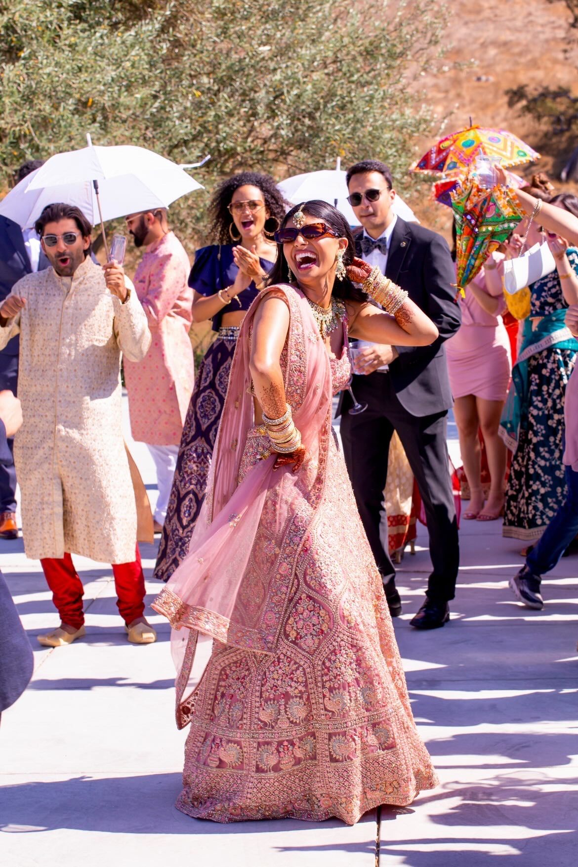 Wedding celebration with guests in colorful attire holding umbrellas and dancing outdoors.