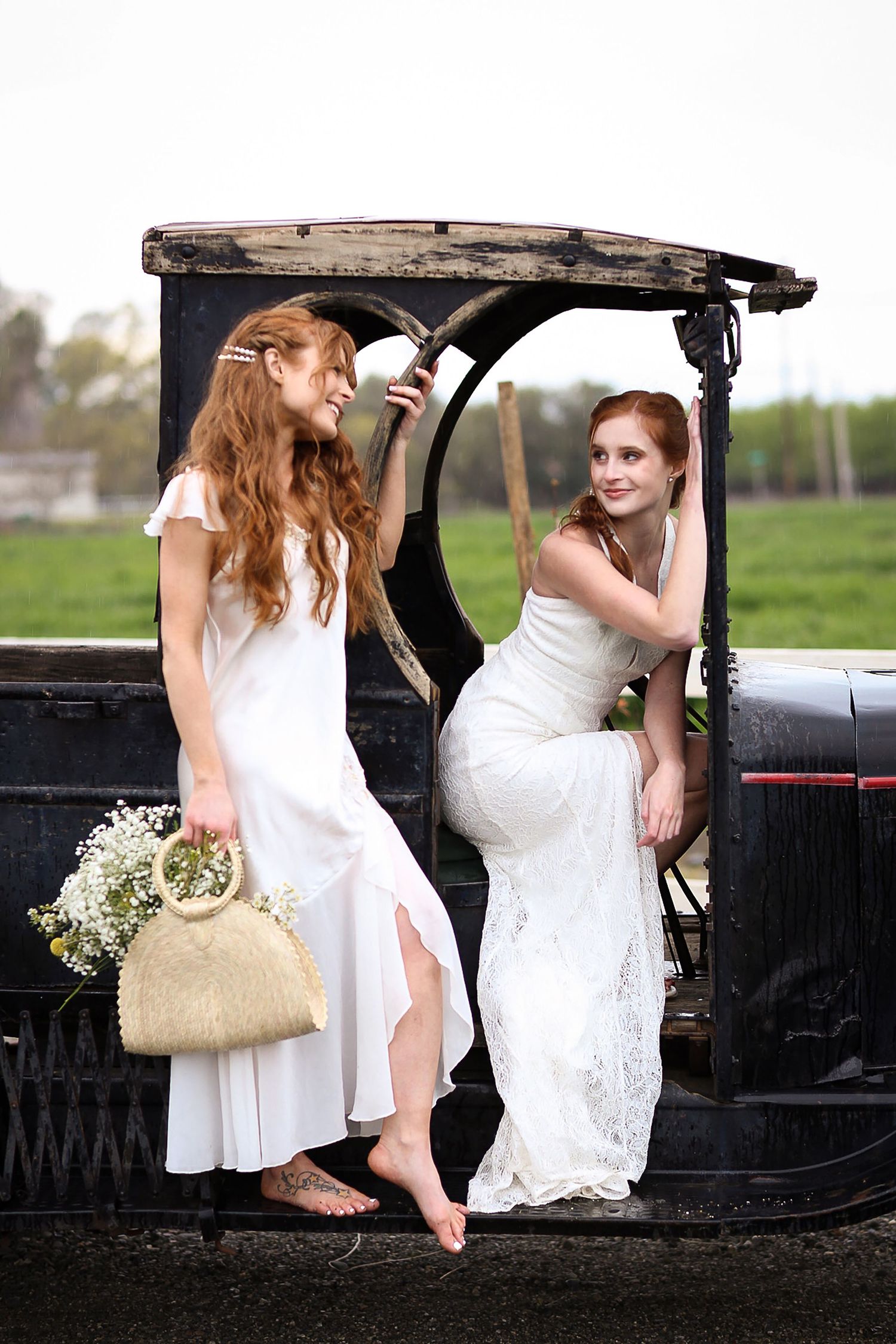 Two women in white dresses posing on vintage black truck for wedding photos.