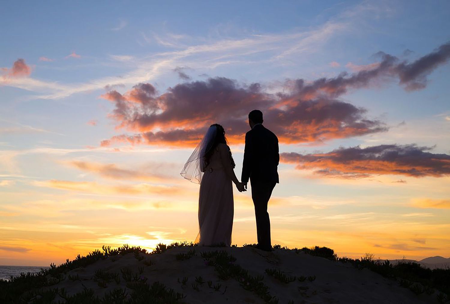 Silhouettes of couple against dramatic sunset sky.