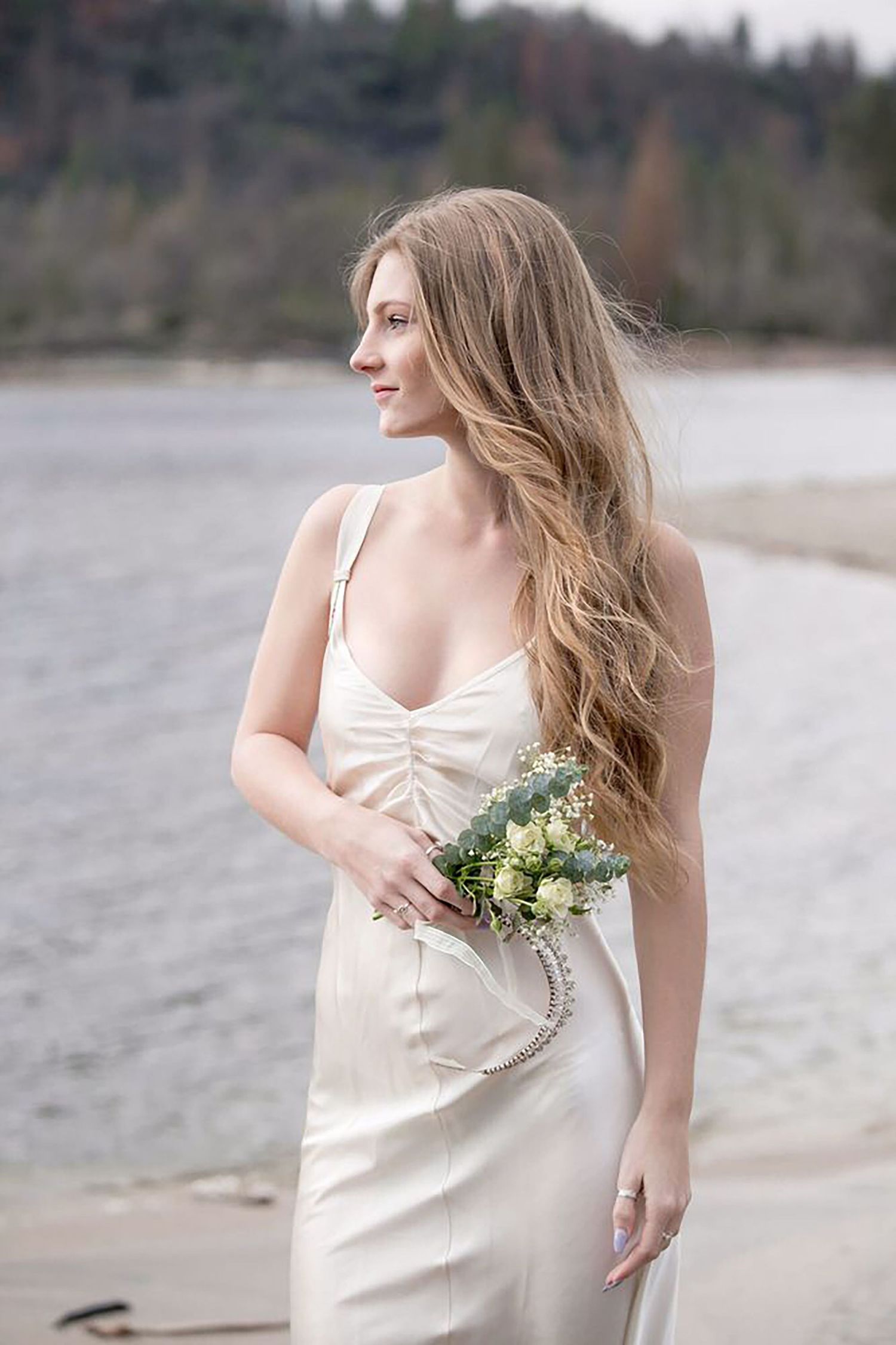 Woman in white slip dress poses gracefully by a lakeside.