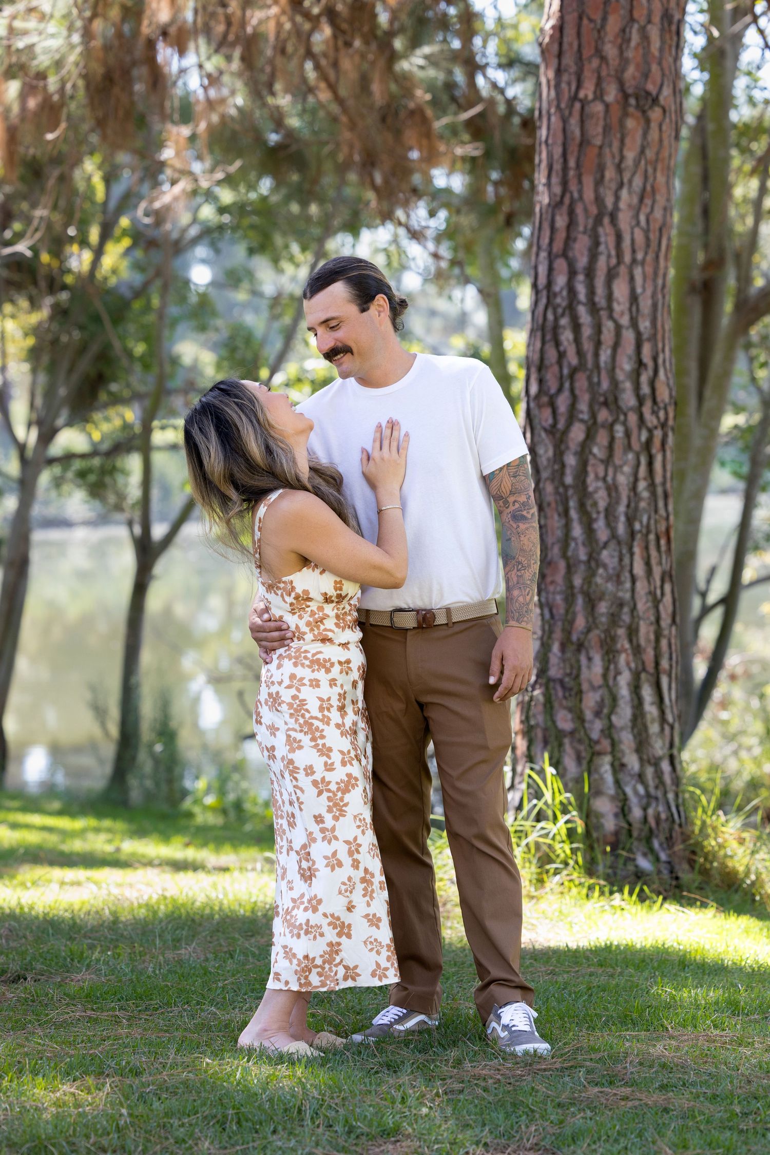 A romantic couple shares tender moments in a sunlit pine forest setting during a photo session.