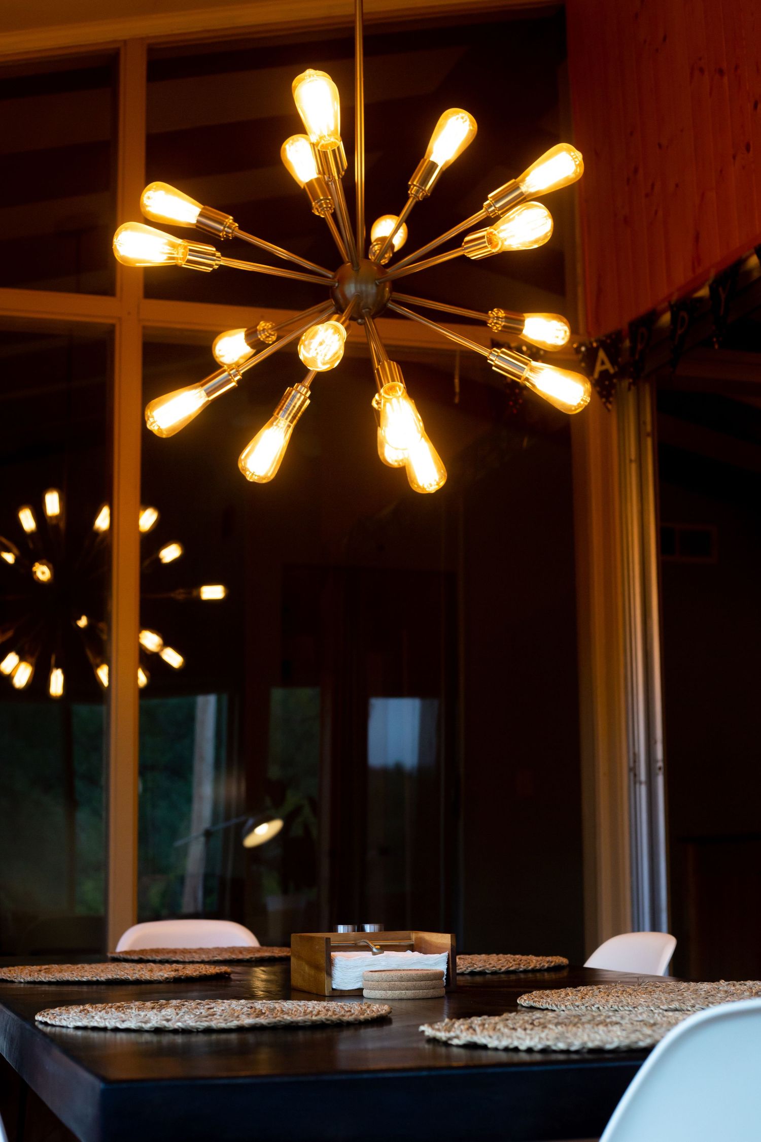 Modern starburst chandeliers with exposed bulbs illuminate a dark interior space with tables below.