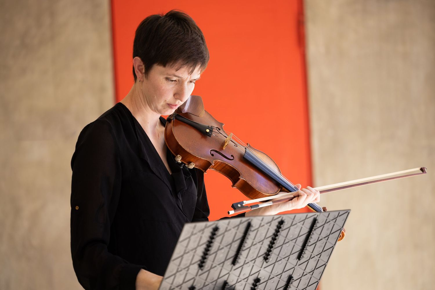 Musician performing with violin against orange backdrop in formal black attire.