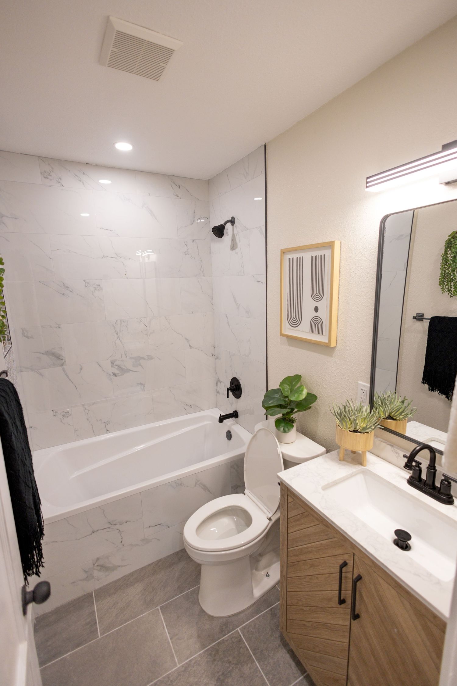 Modern bathroom with marble walls, wood vanity, white countertop, and gray tile floors featuring sleek black fixtures.