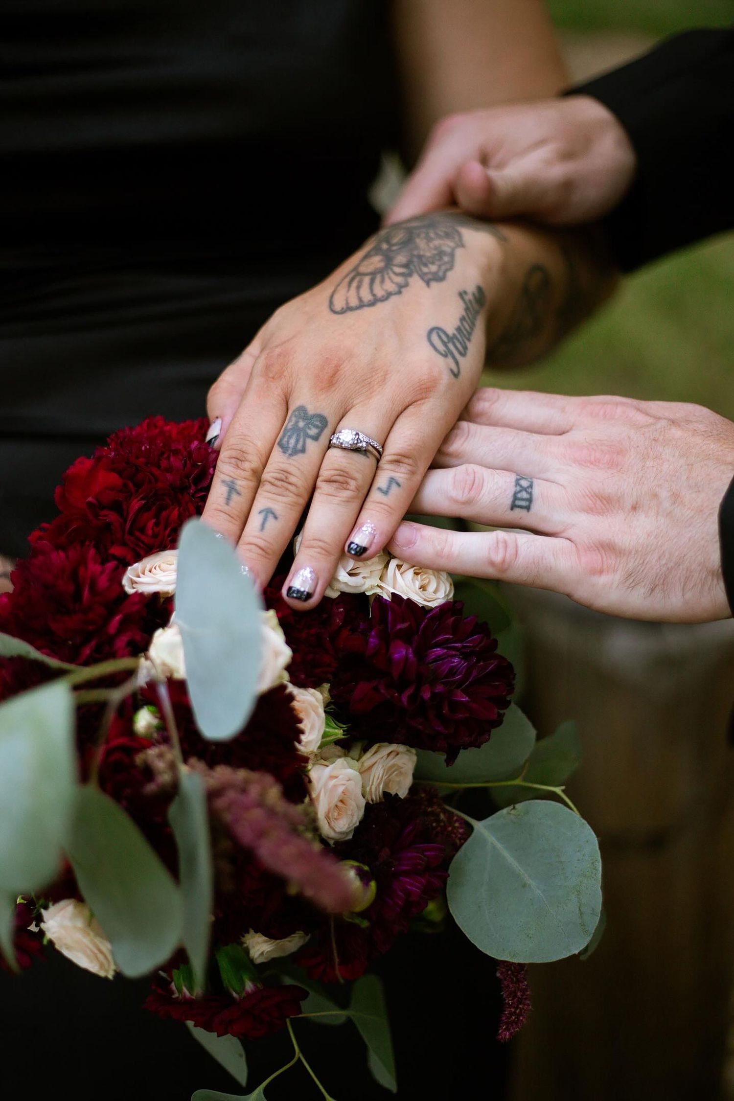 Tattooed hands arranging deep red and blush flowers with eucalyptus leaves.