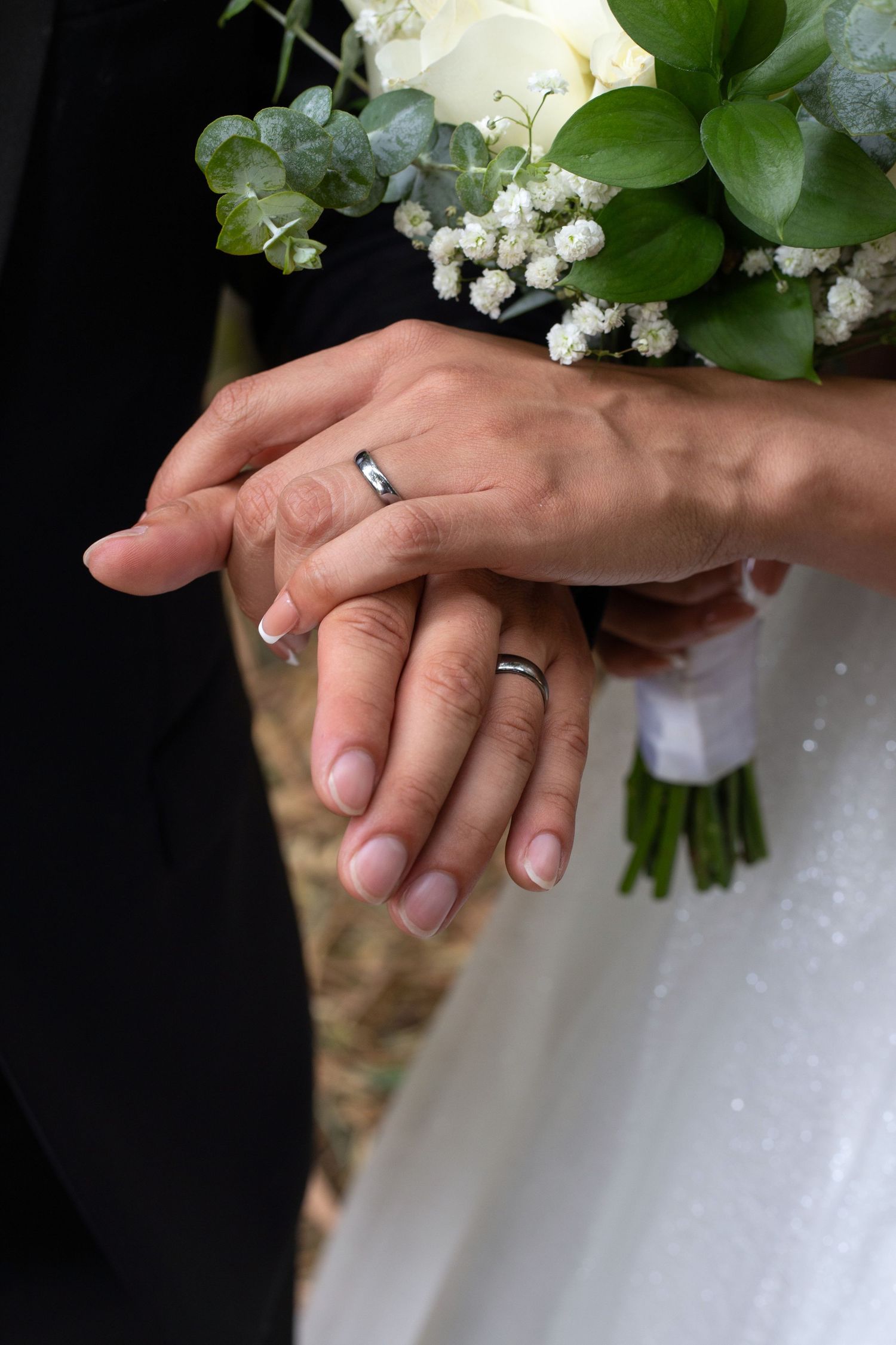 Close up of hands holding white floral bouquet with wedding rings.