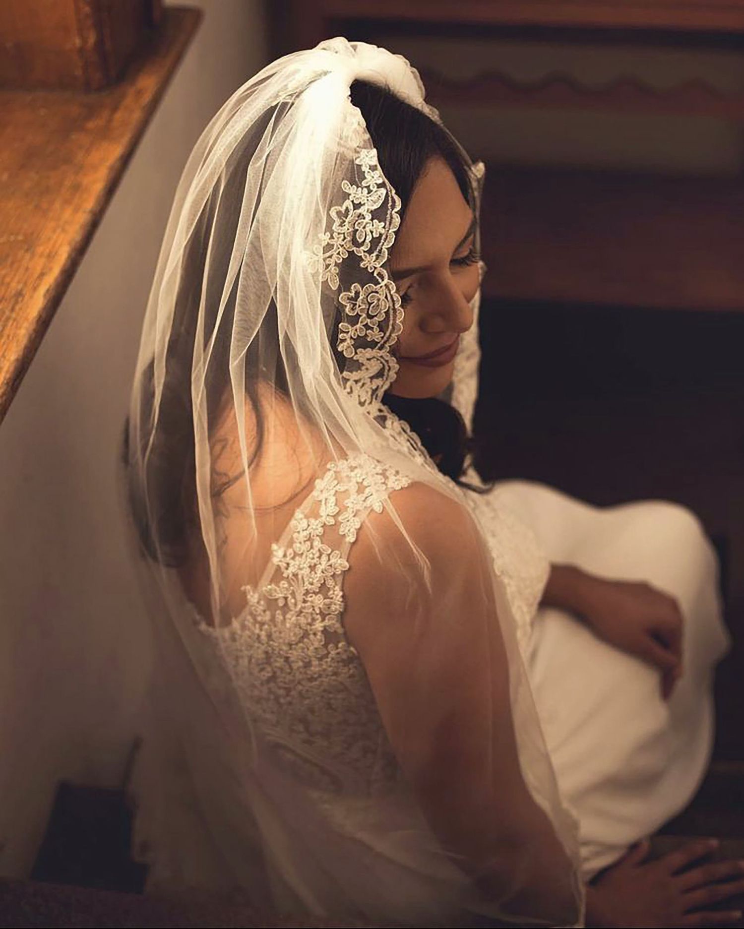Bride wearing delicate lace veil in romantic indoor setting.