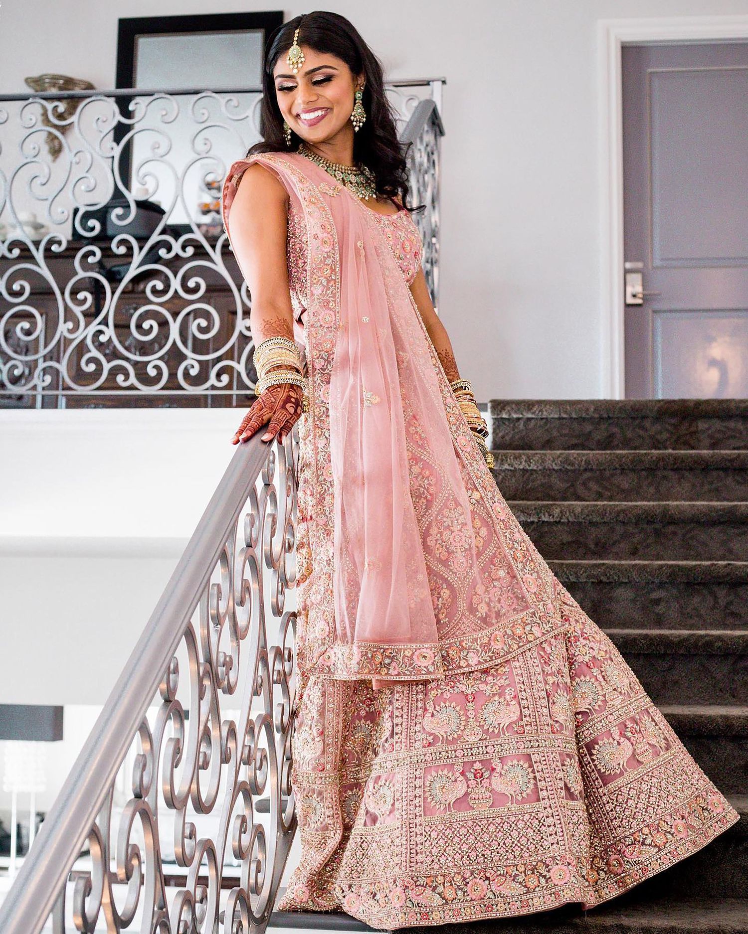 Person twirling in pink embellished lehenga on white staircase with ornate railing.