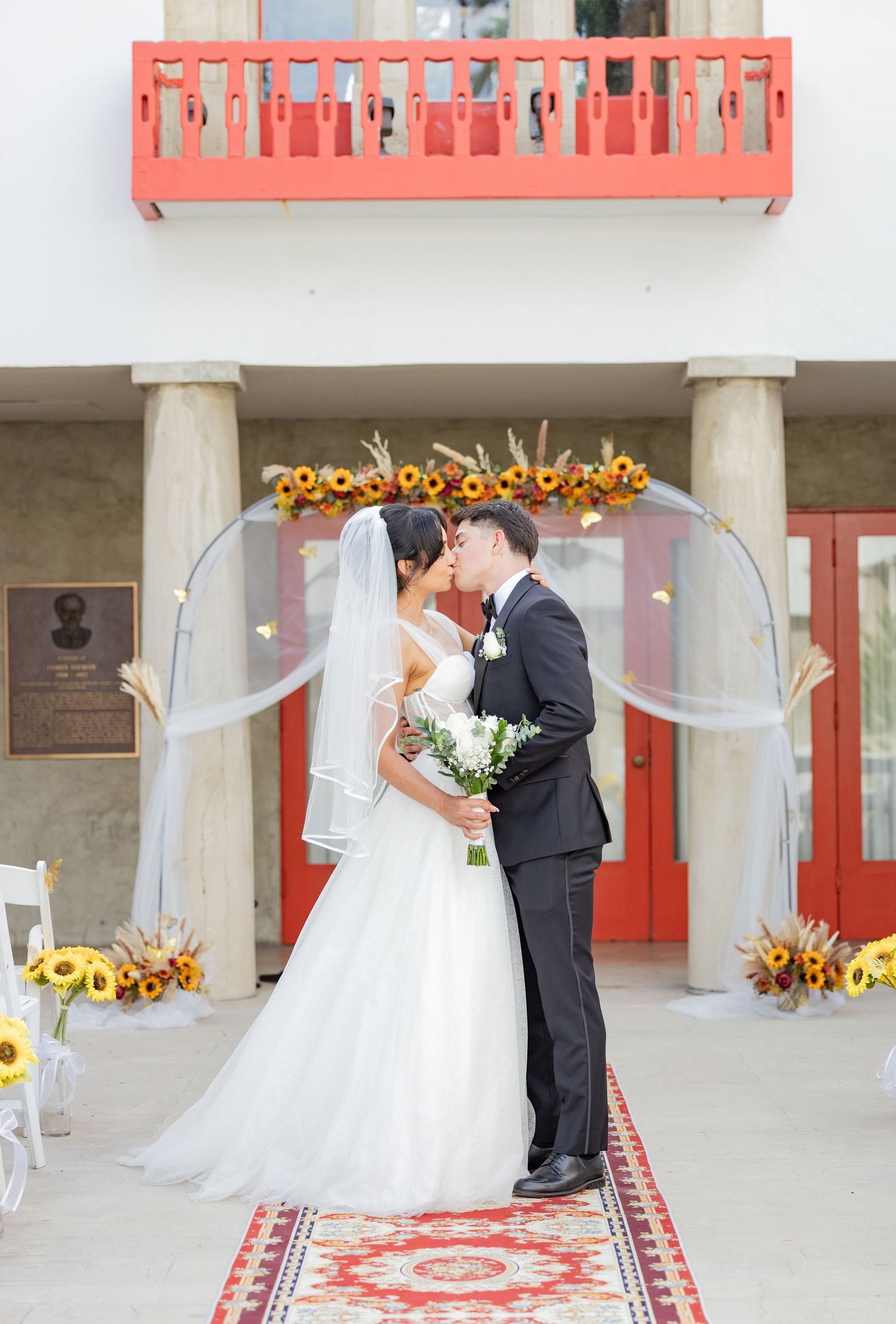 Wedding ceremony setup with red doors, sunflower decorations and oriental rug.