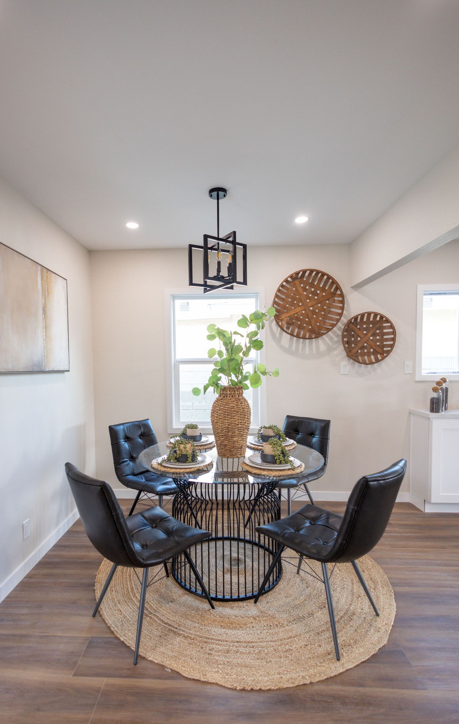 Modern dining area with blue velvet chairs, round black table, and natural jute rug under warm lighting.