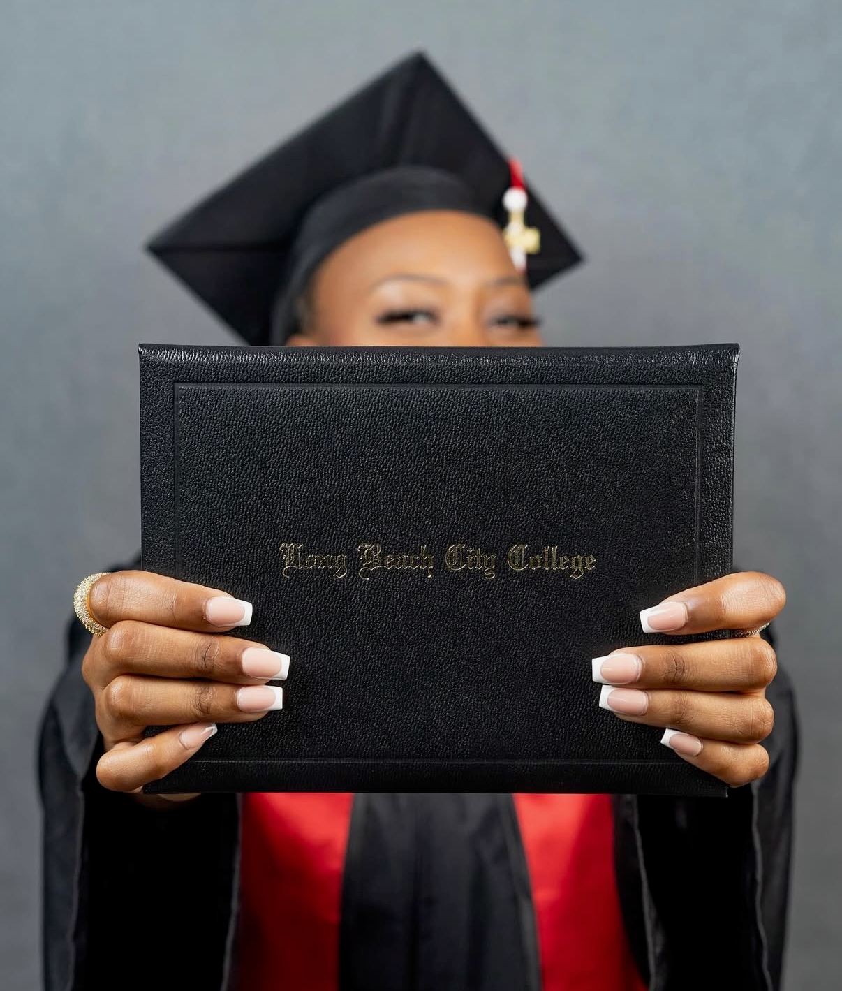 Graduate in cap and gown holds up a Long Beach City College diploma case during graduation ceremony.