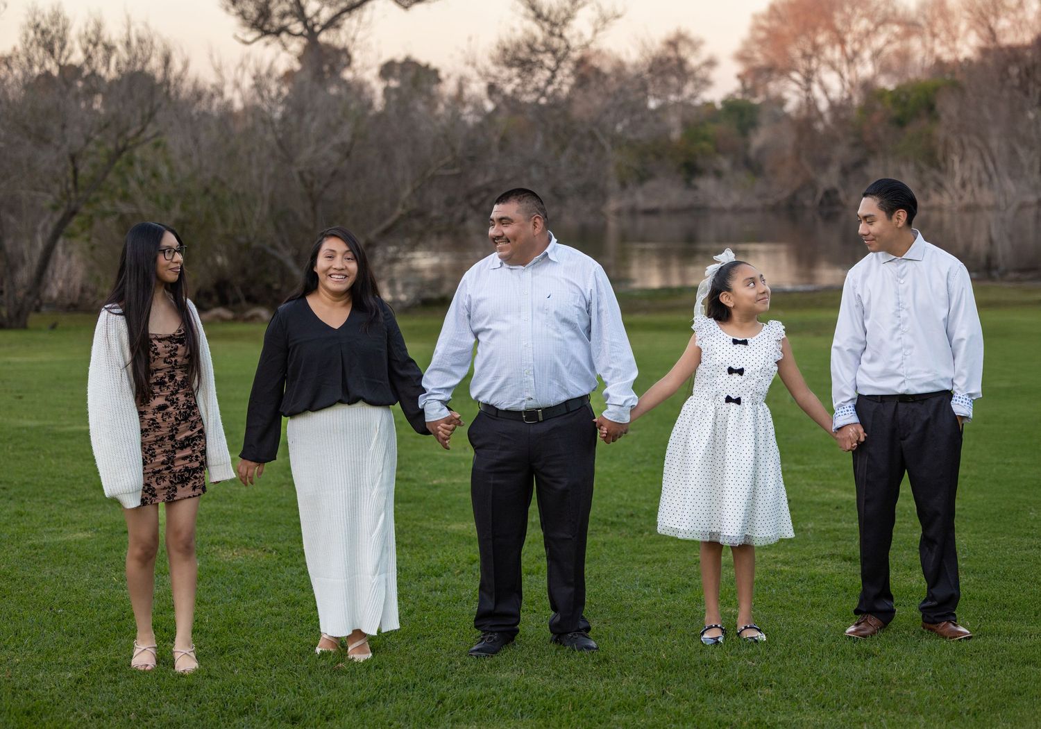 A group of five people standing together on a grassy lawn at sunset.