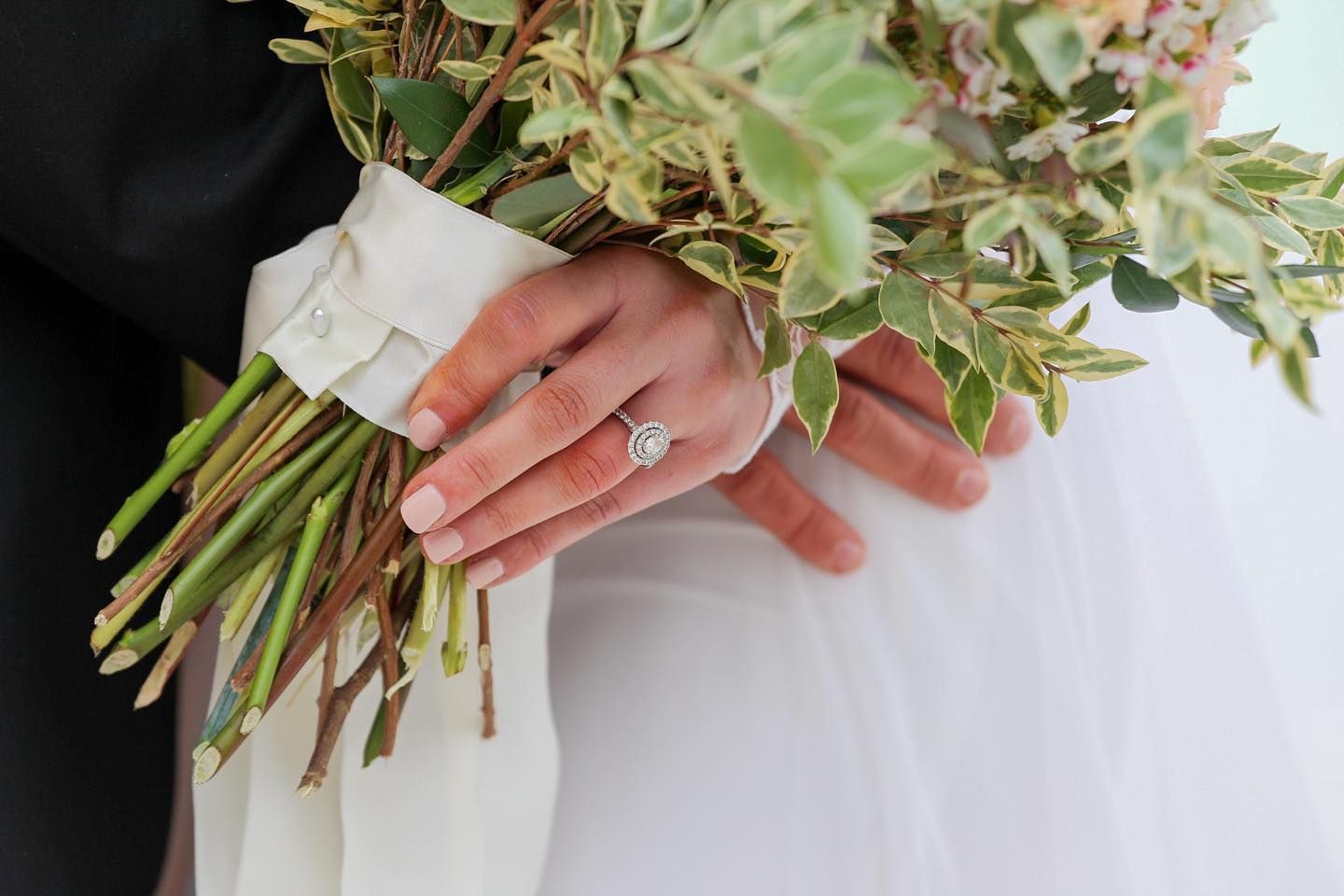 Close up of hands holding a rustic bouquet with greenery and a diamond engagement ring.