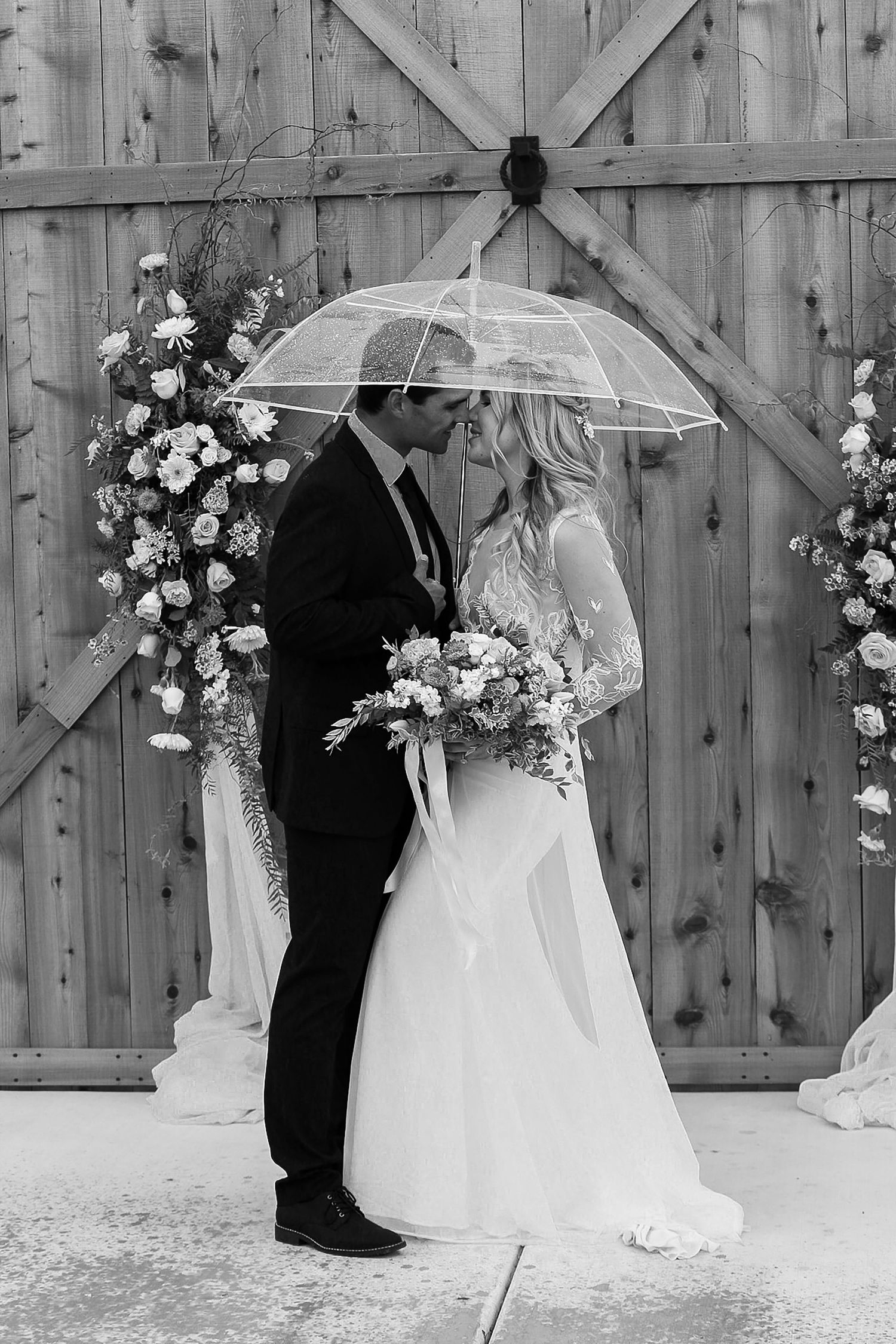 Black and white wedding photos with clear umbrellas against rustic wooden barn backdrop.