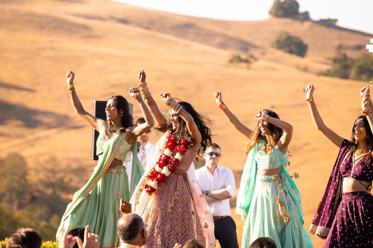 Wedding party in pastel dresses celebrating against golden hillside backdrop.