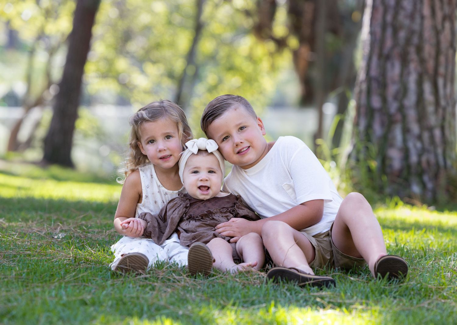 Family photo session captured on grass under pine trees in natural outdoor setting.
