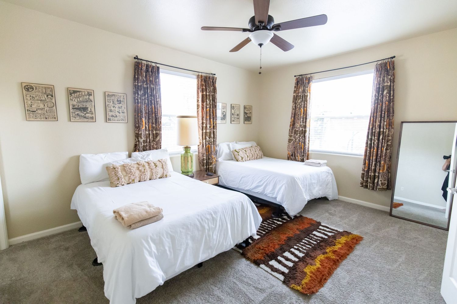 Panoramic view of a bright bedroom with white bedding, floral curtains, and a ceiling fan mounted above.
