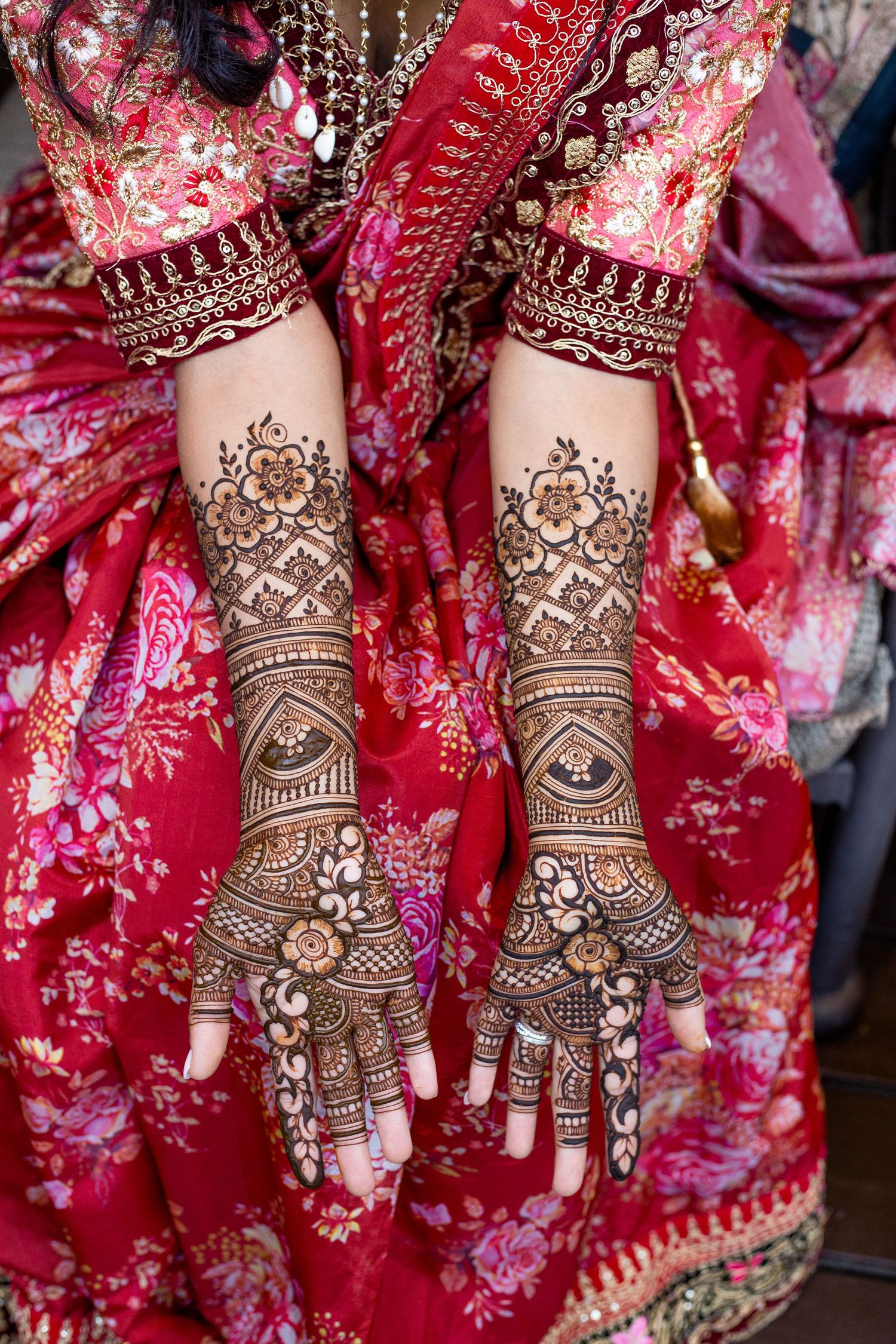 Intricate henna designs adorn hands against red traditional wedding attire.