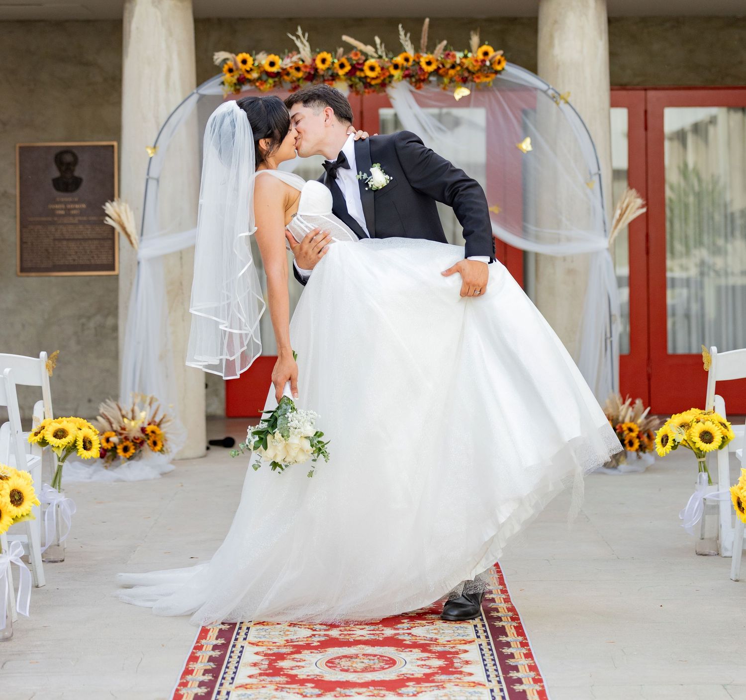 Wedding couple poses with white umbrellas and sunflowers in an elegant outdoor venue setting.