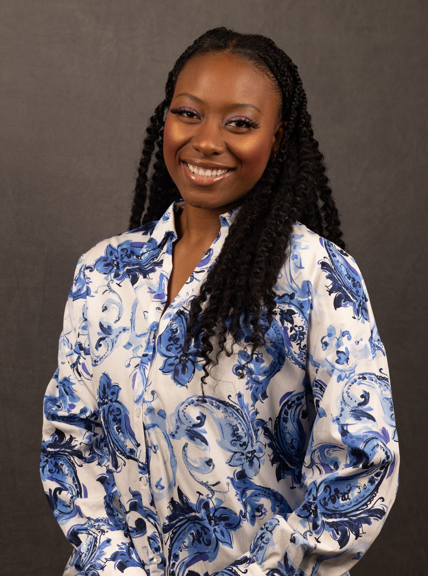 Professional studio portrait featuring a bright blue and white floral print blouse and long braided hairstyle against gray backdrop.