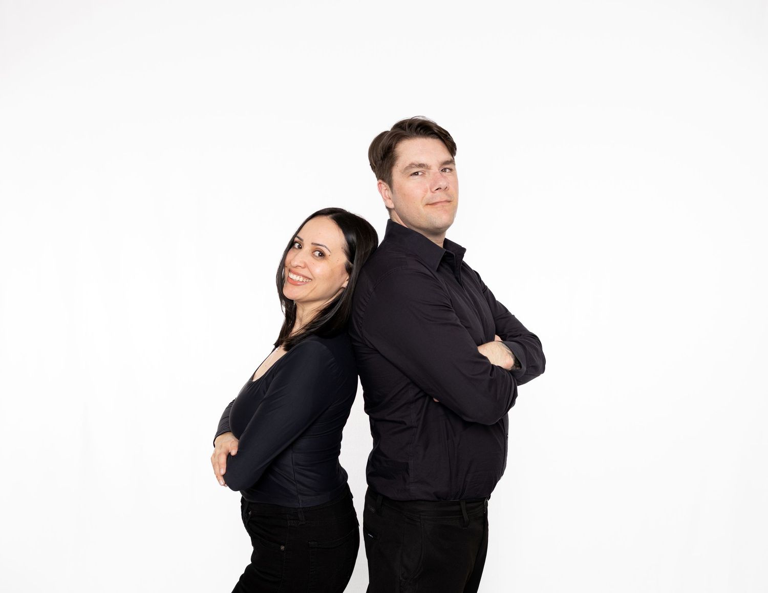 Two business professionals in black attire stand back-to-back with contrasting poses and expressions.