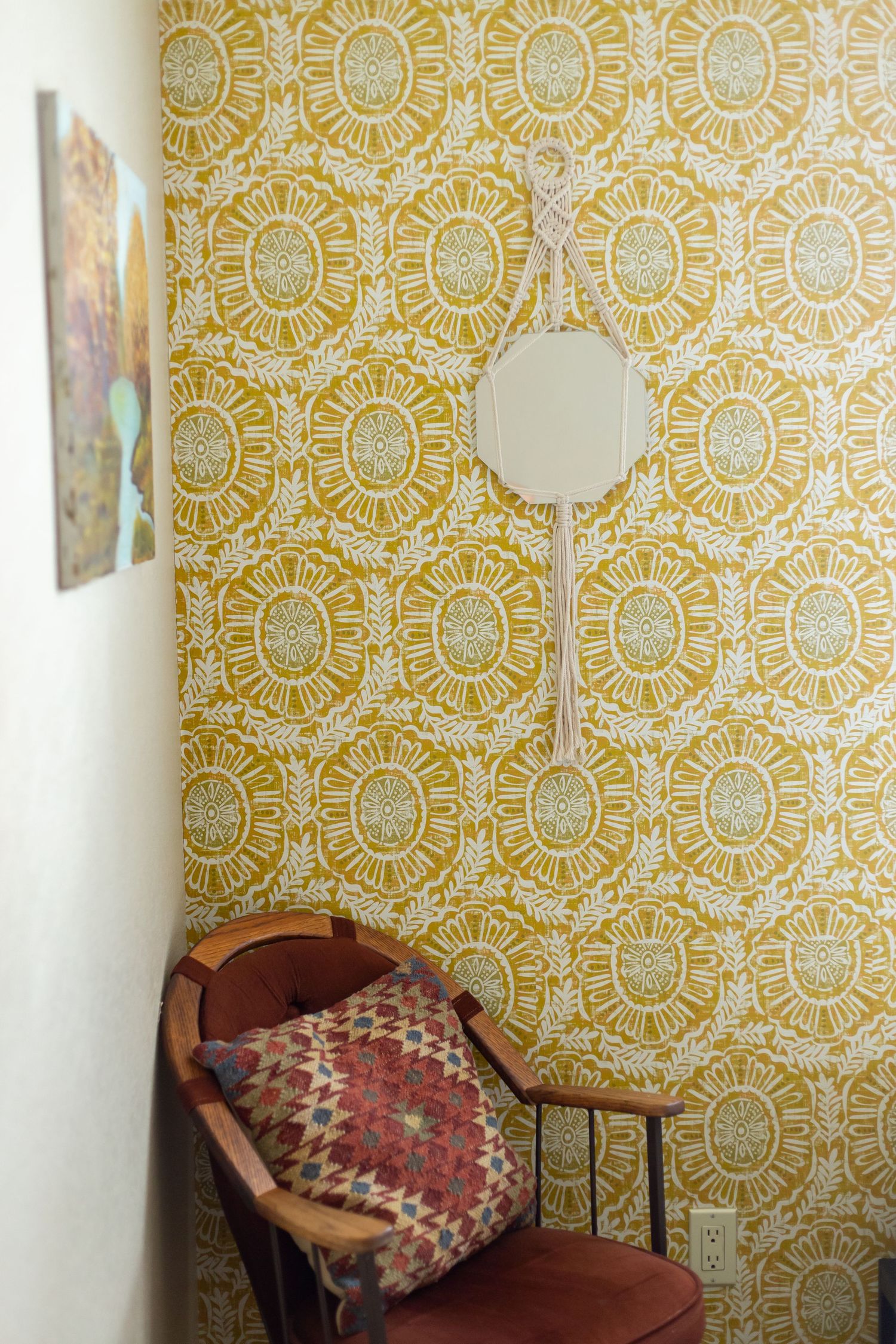 A vintage chair sits against a wall covered in retro yellow sunburst pattern wallpaper with a decorative pillow.