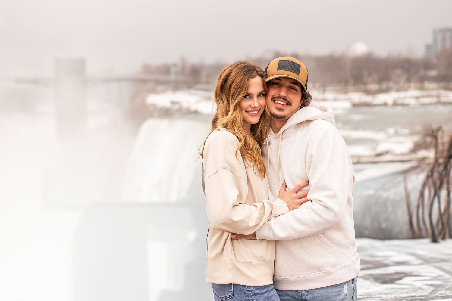 Newly engaged couple hug in front of Niagara Falls, New York after the surprise proposal during their engagement session.