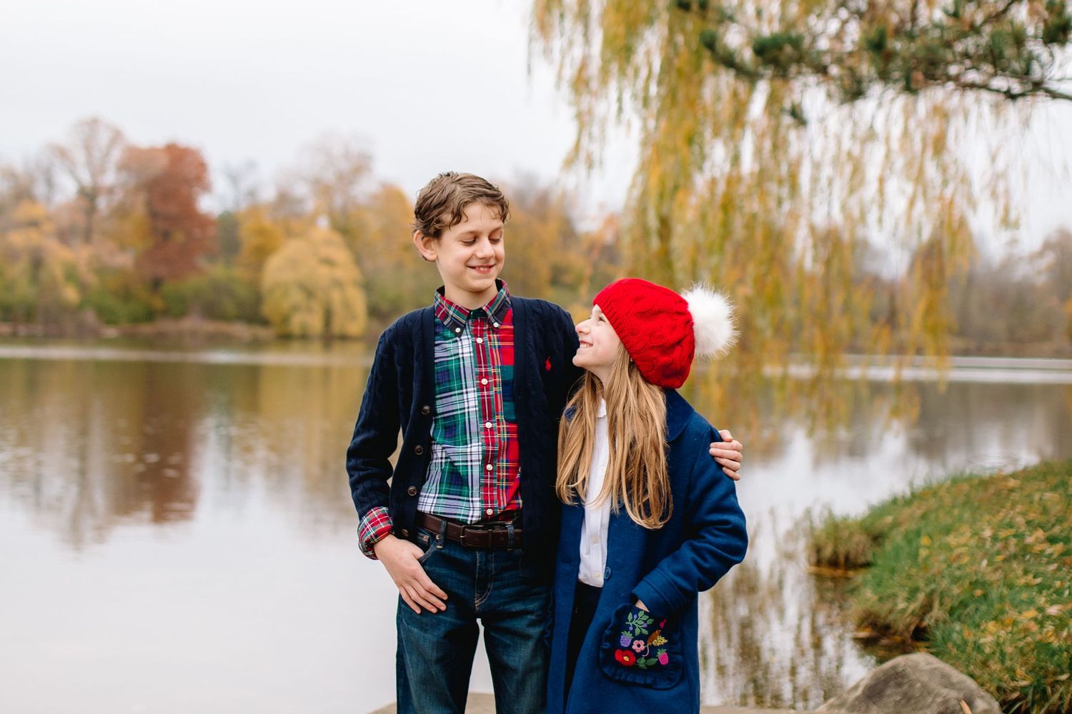 Brother and sister pose looking at each other at Delaware Park at Hoyt Lake in Buffalo during their family portrait session.