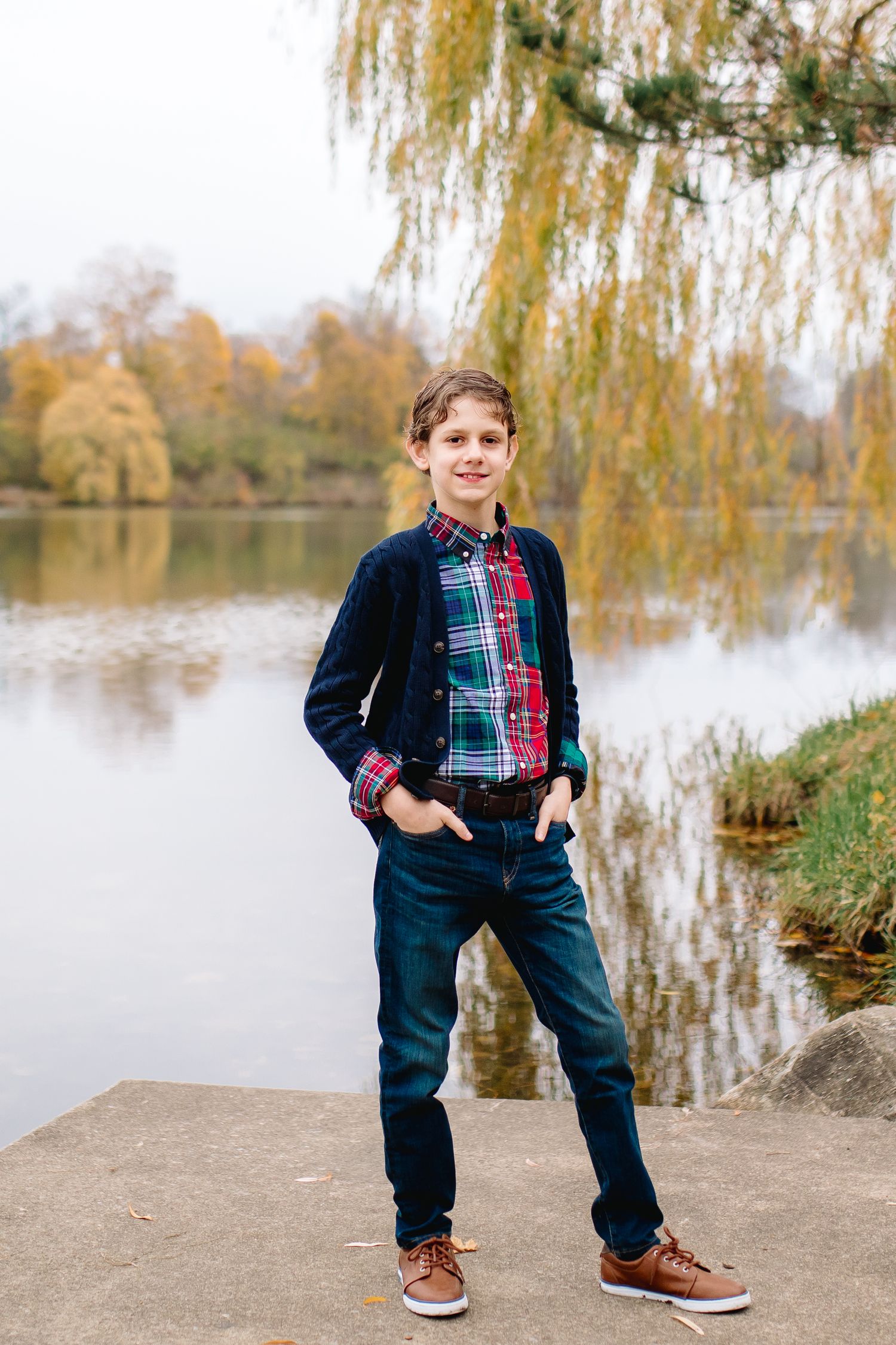 12 year old boy poses in front of willow tree at hoyt lake in delaware park in Buffalo New York during family portrait session.