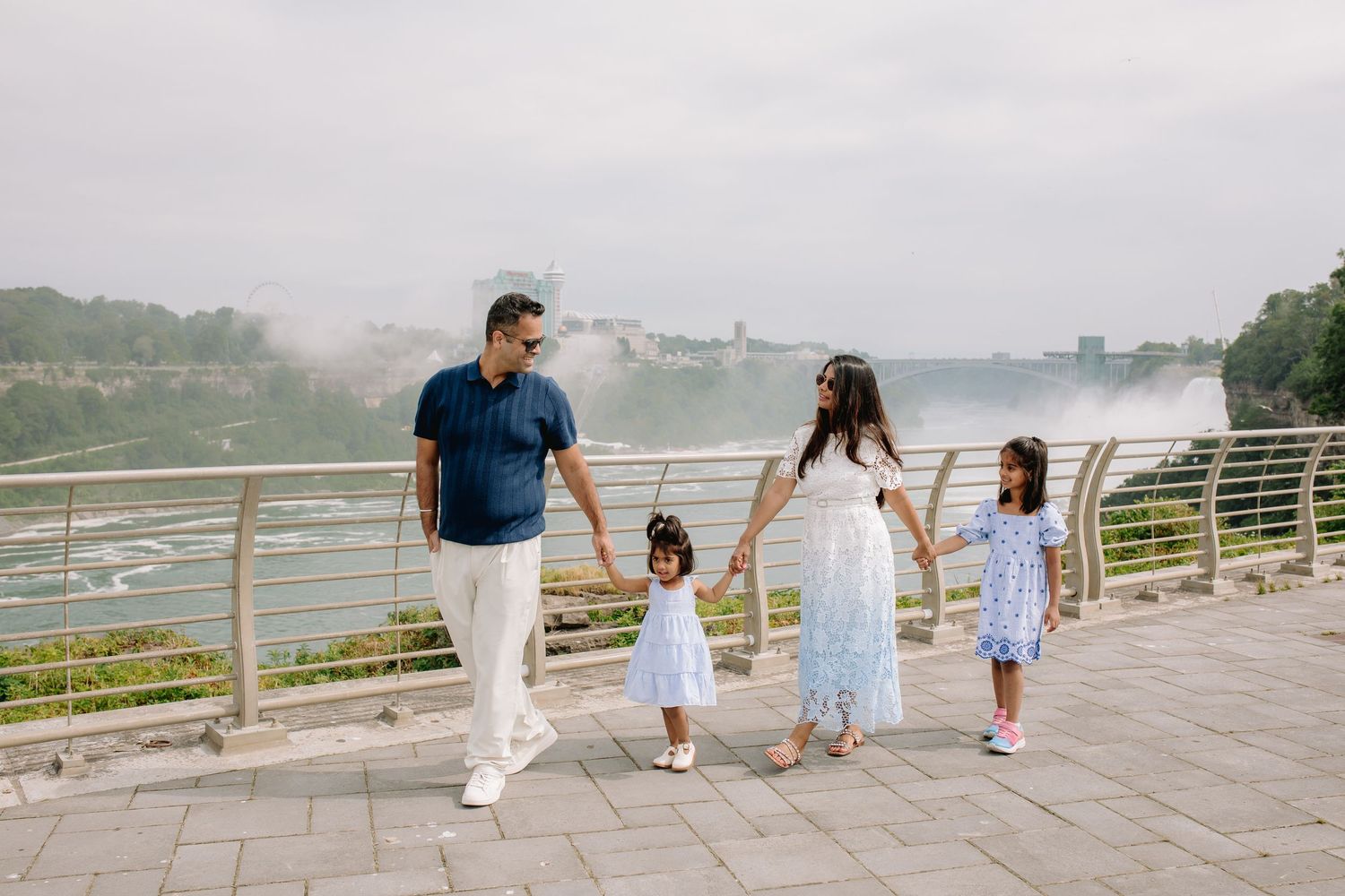 Family of four holds hands and walks in front of Niagara Falls, New York.
